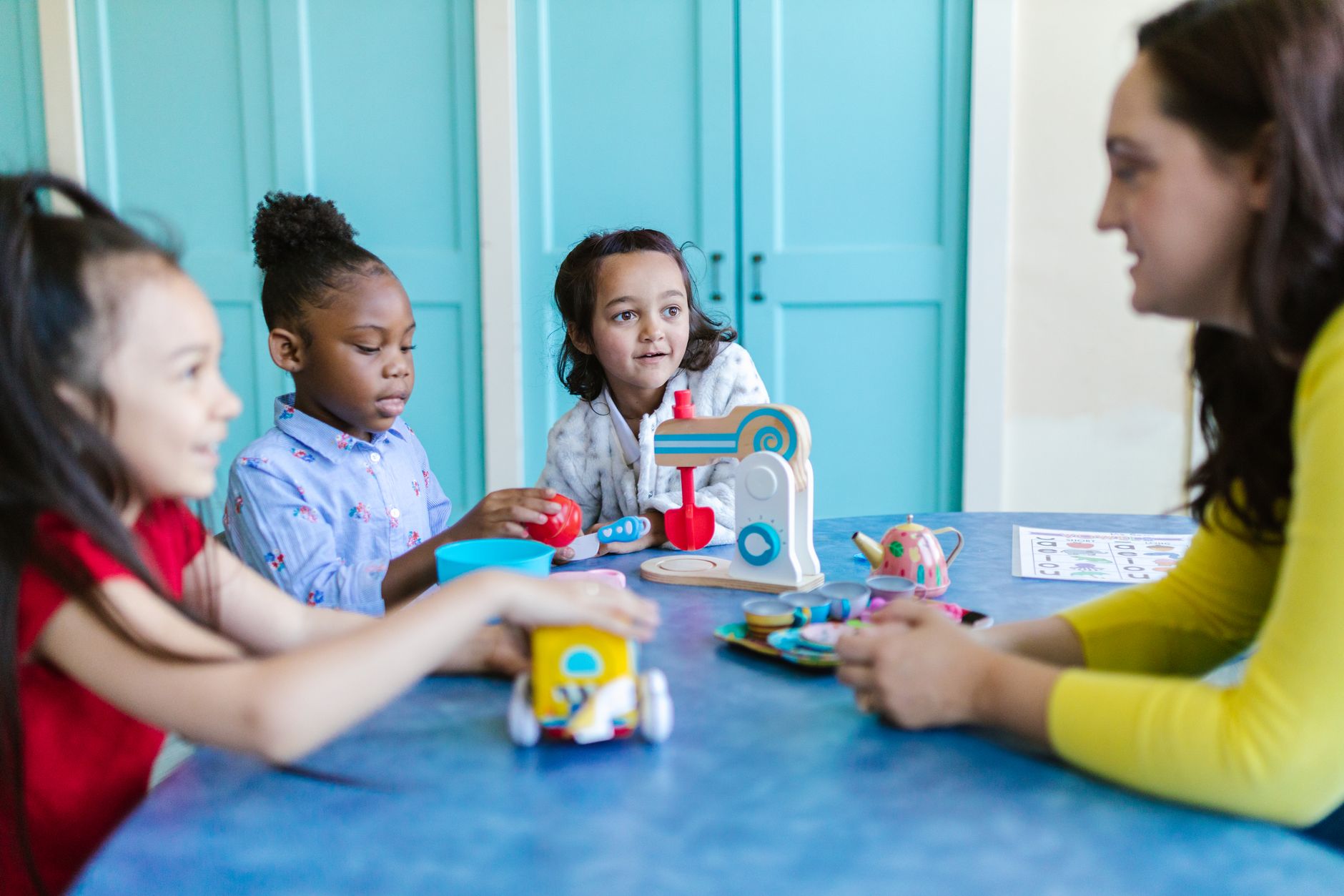 Young children engaged in play with toys and a teacher in a colorful preschool setting.