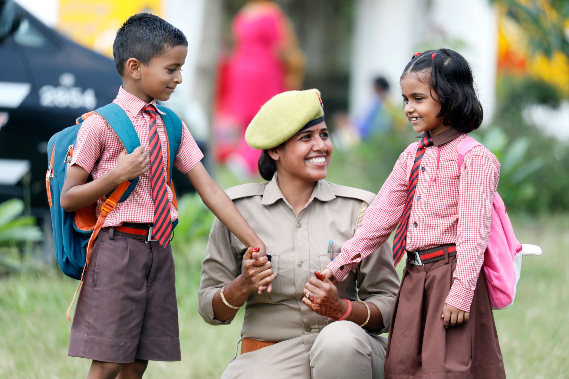 A policewoman smiling and interacting with schoolchildren in uniforms. Outdoors, warm and cheerful scene.
