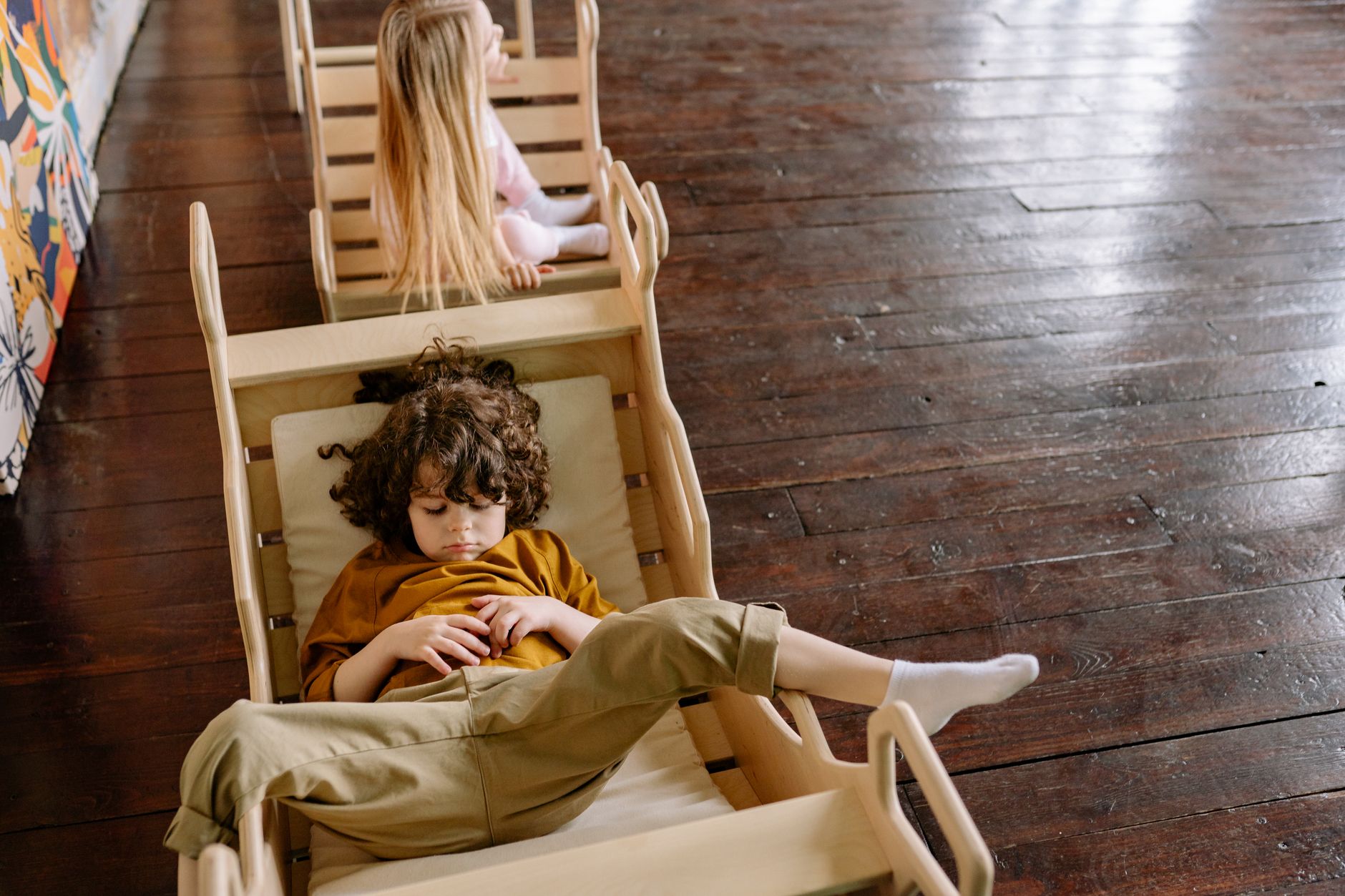 Two children resting on wooden chairs indoors with a peaceful atmosphere.