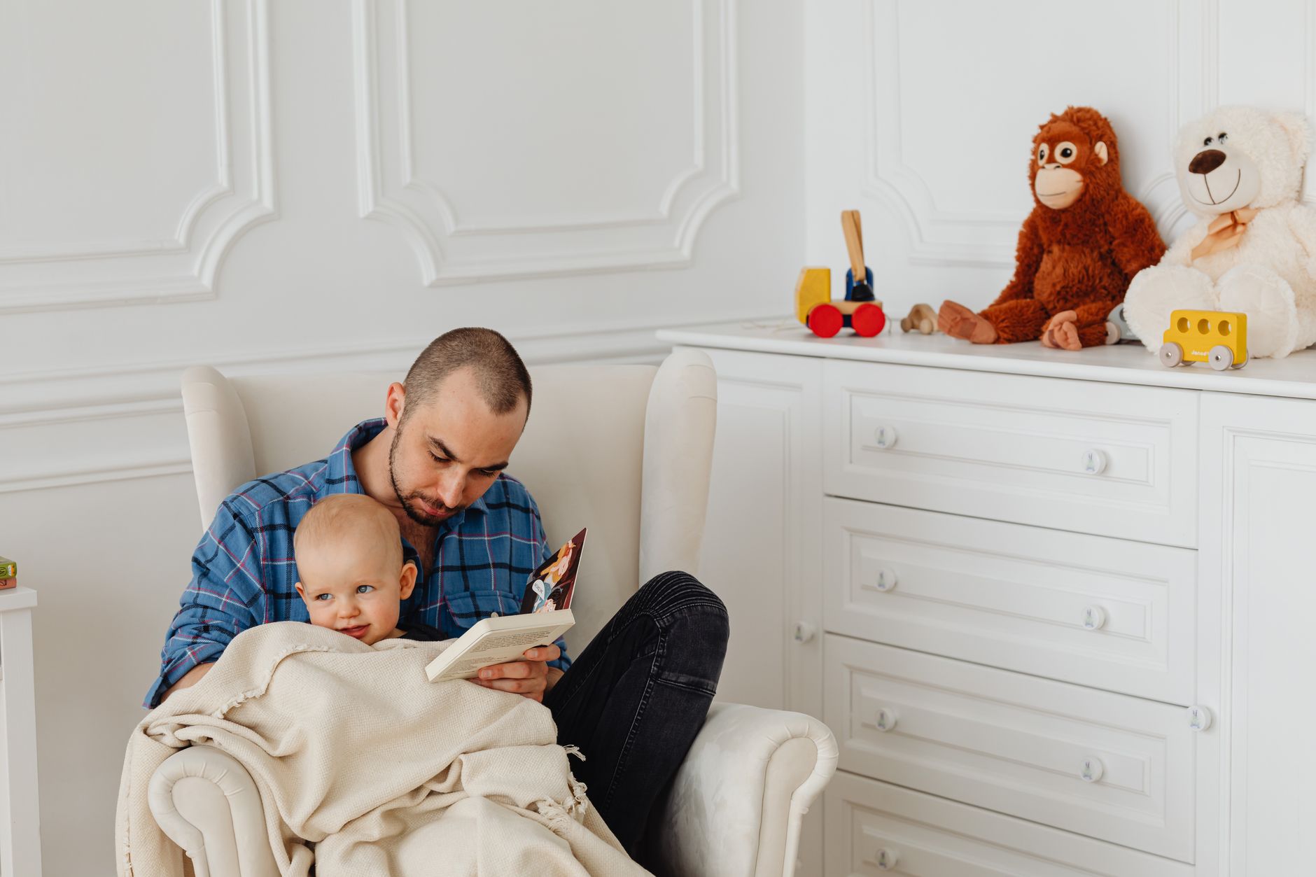A father and baby bonding while reading in a cozy, toy-filled nursery.