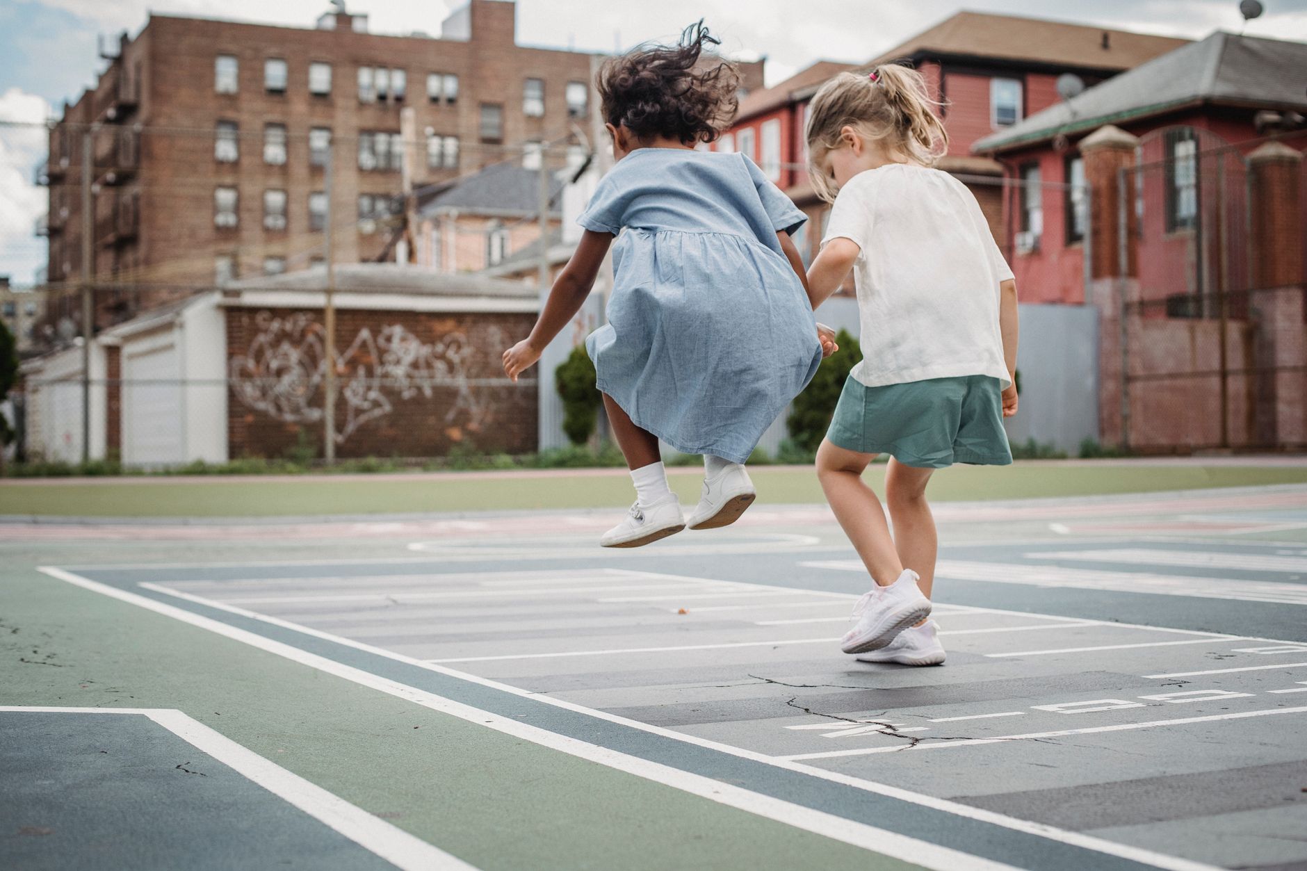 Two young girls jumping and playing together on a city playground.