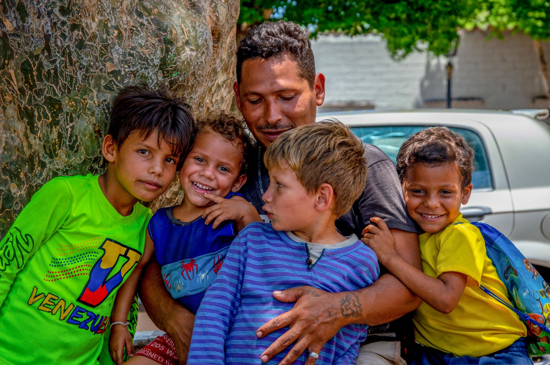 A joyful family moment as a father hugs his smiling children outdoors.