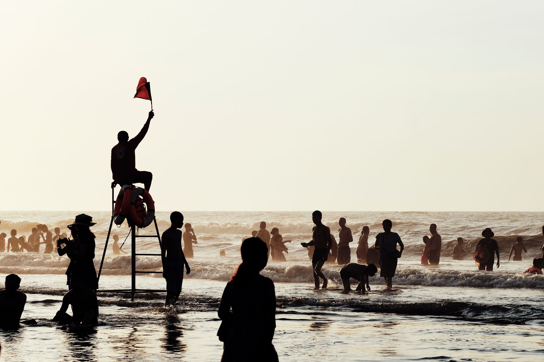 Sundrenched Vietnamese beach with silhouettes of diverse people enjoying the ocean under lifeguard watch.