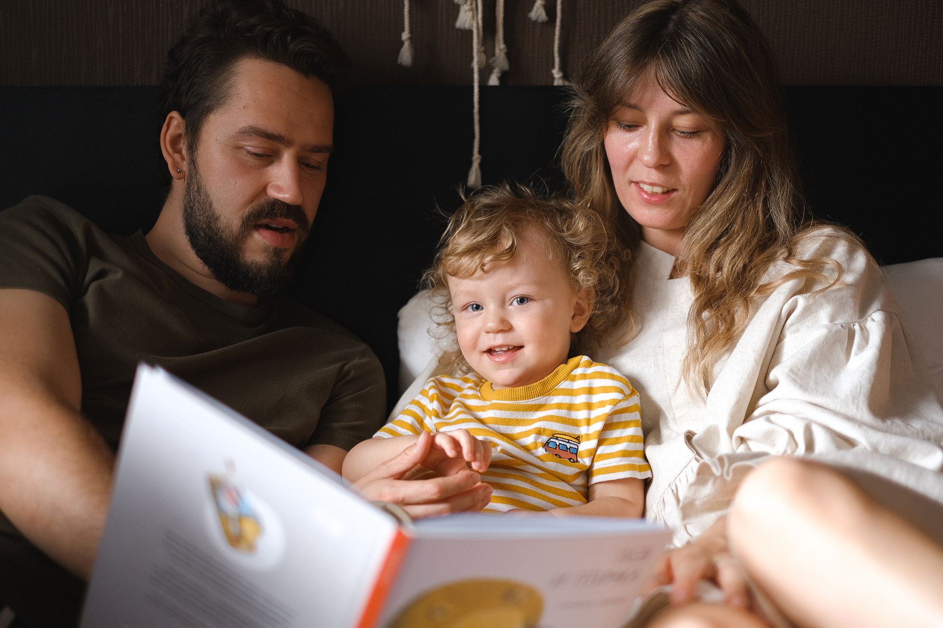 A happy family reading together, featuring parents and their smiling child enjoying a book indoors.