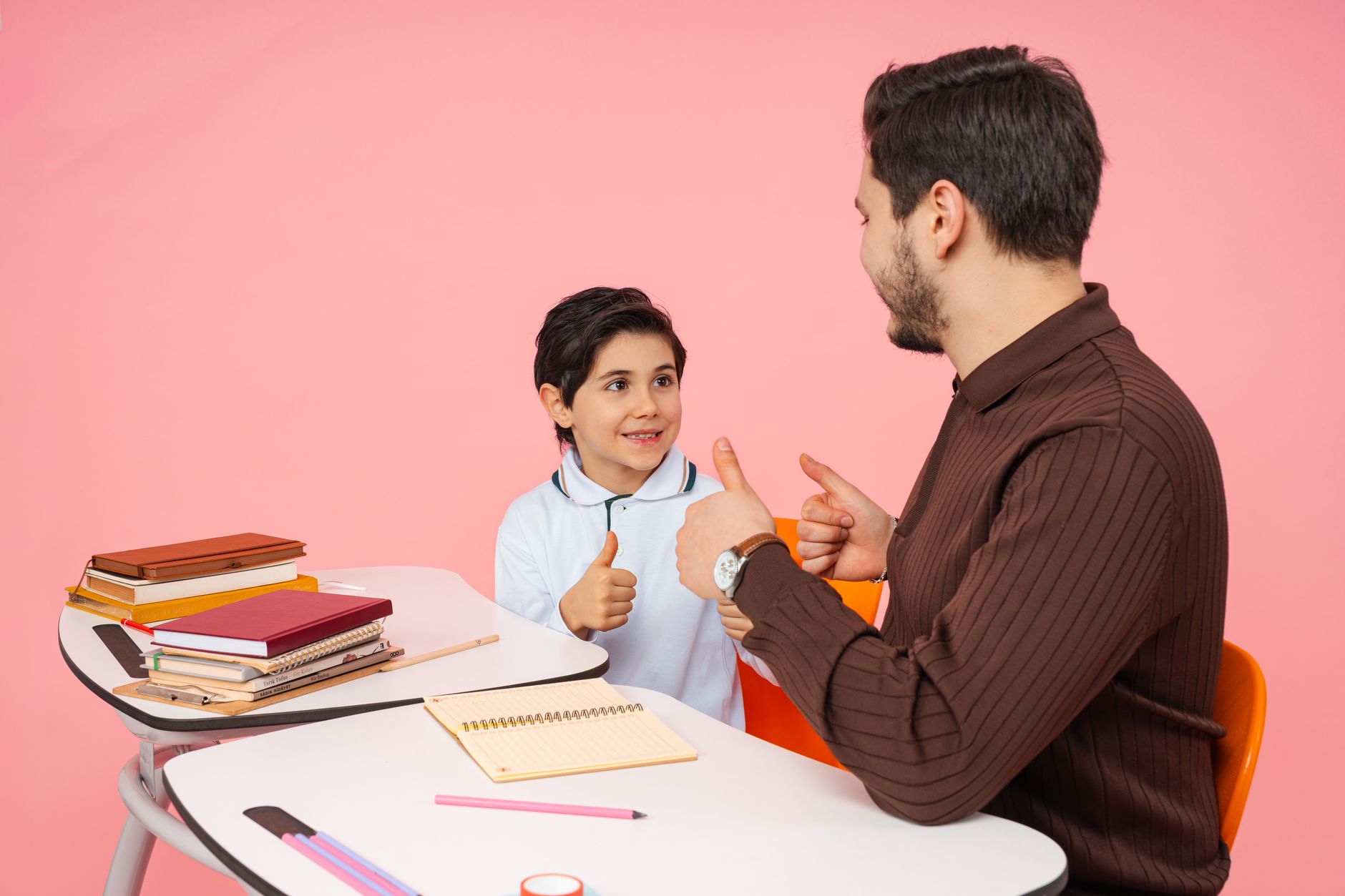 A teacher and student exchange thumbs up in a classroom setting, illustrating positive reinforcement.