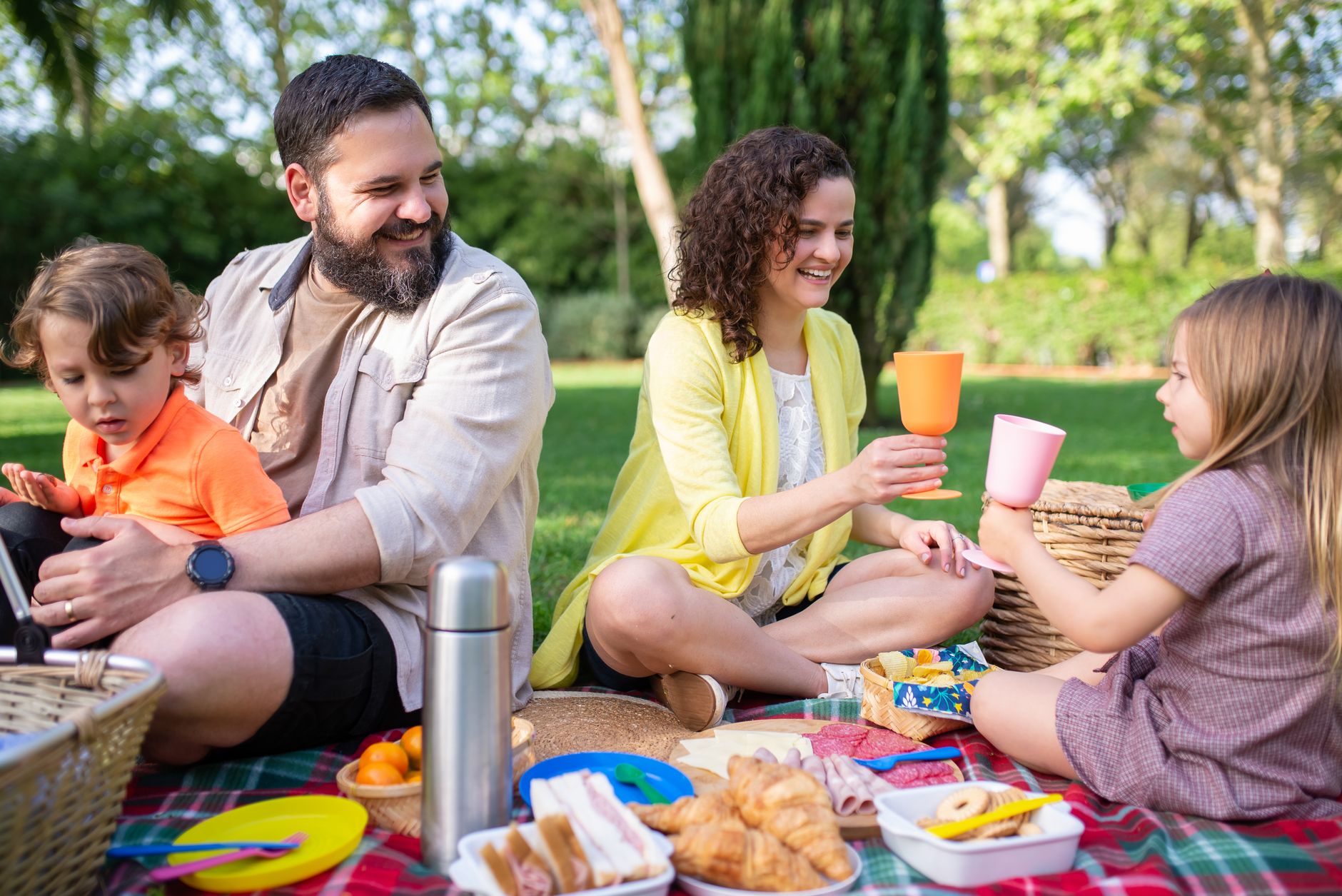 A joyful family enjoying a picnic outdoors with snacks and drinks on a sunny day.