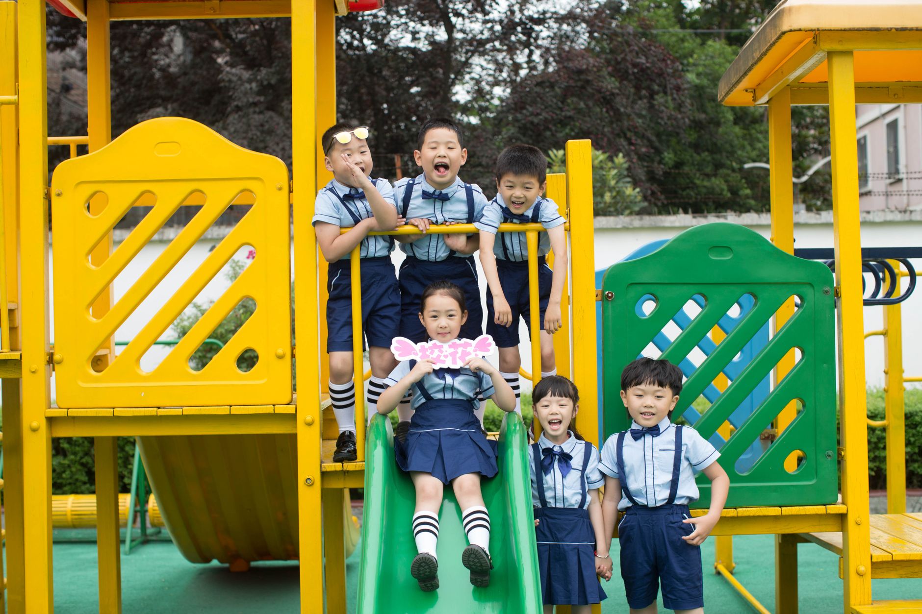 Joyful children in school uniforms playing on colorful playground equipment outdoors.