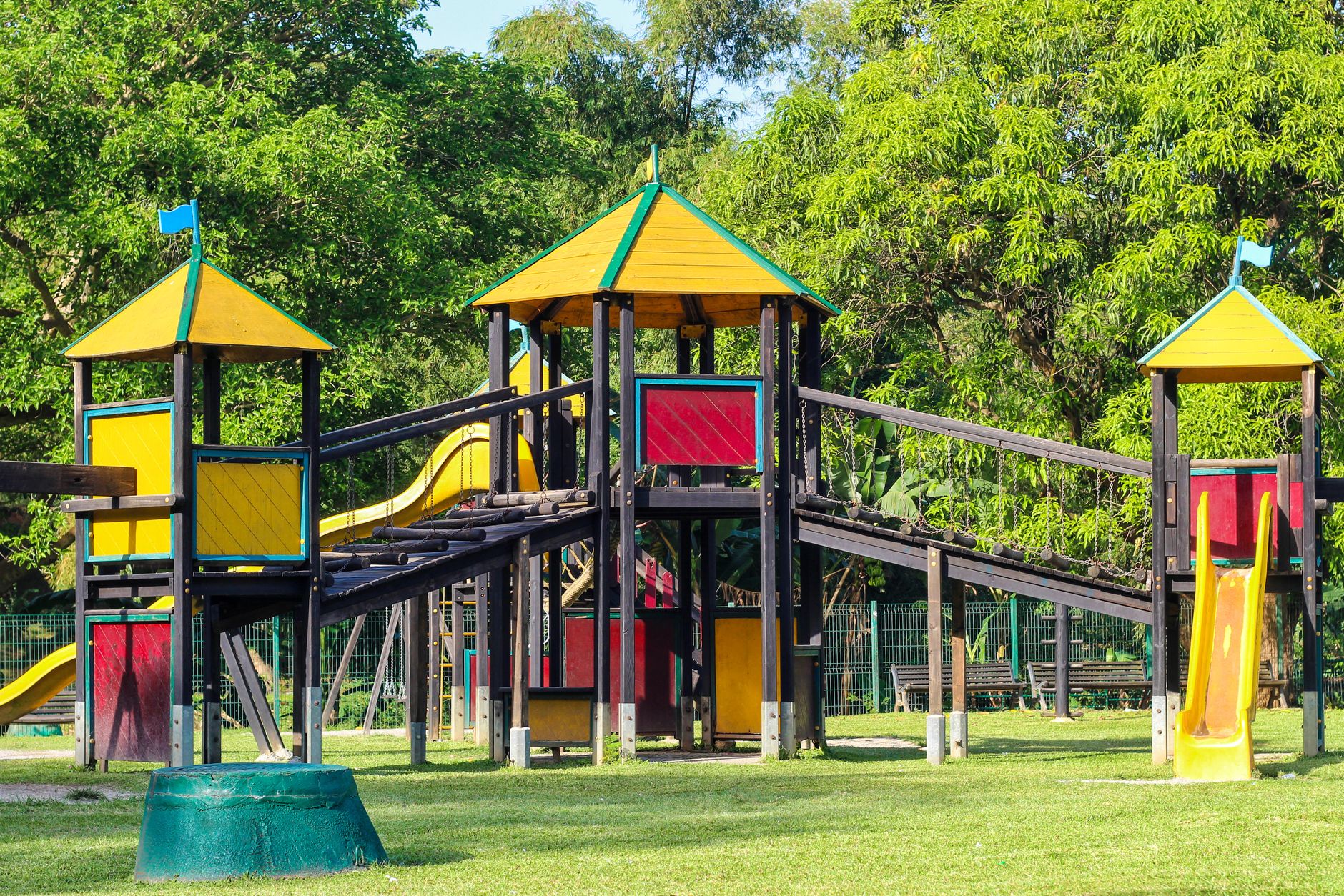 A colorful playground with vibrant slides surrounded by lush green trees in a sunny park.