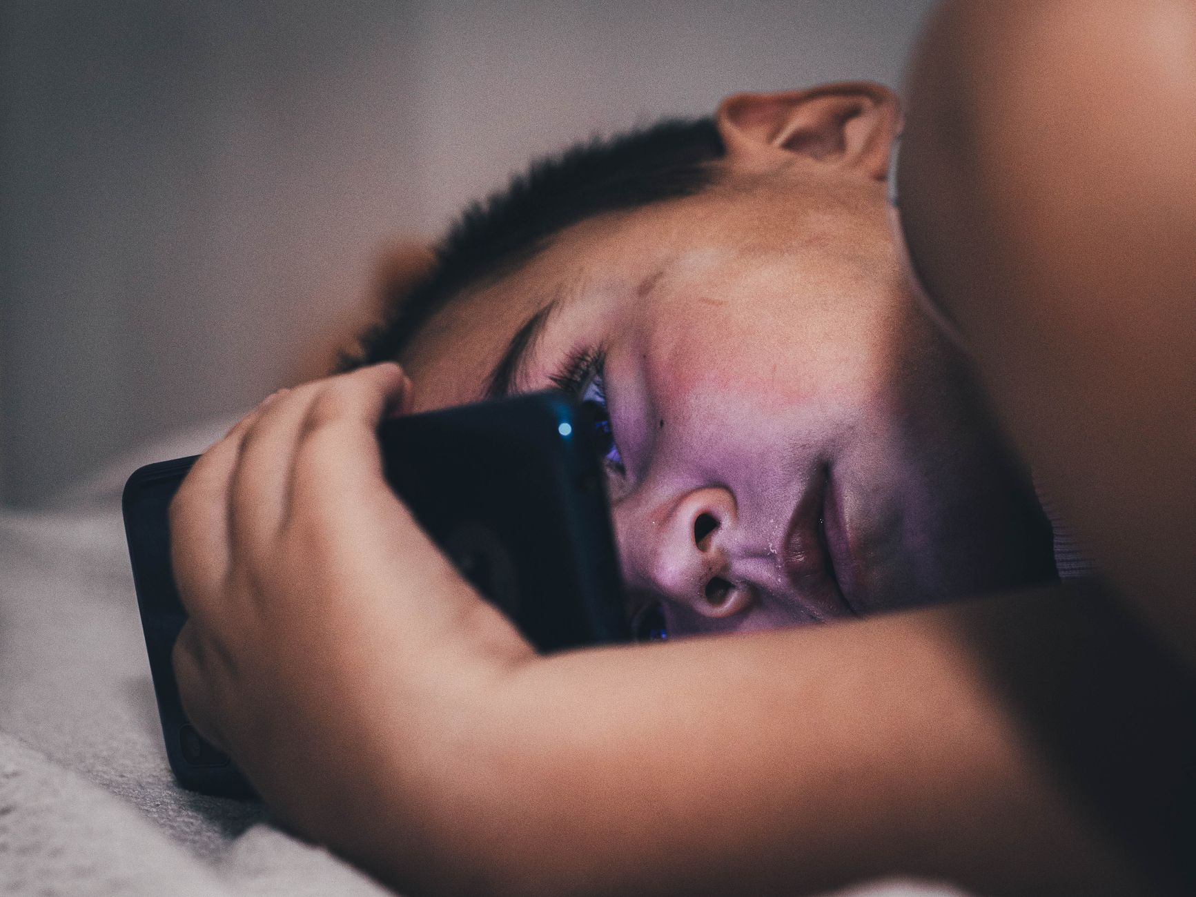 Close-up of a teenager using a smartphone at night, creating a moody atmosphere.