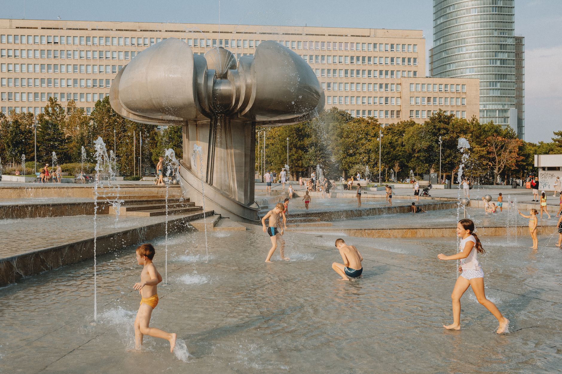 Children enjoying a sunny day playing at a modern urban fountain park.