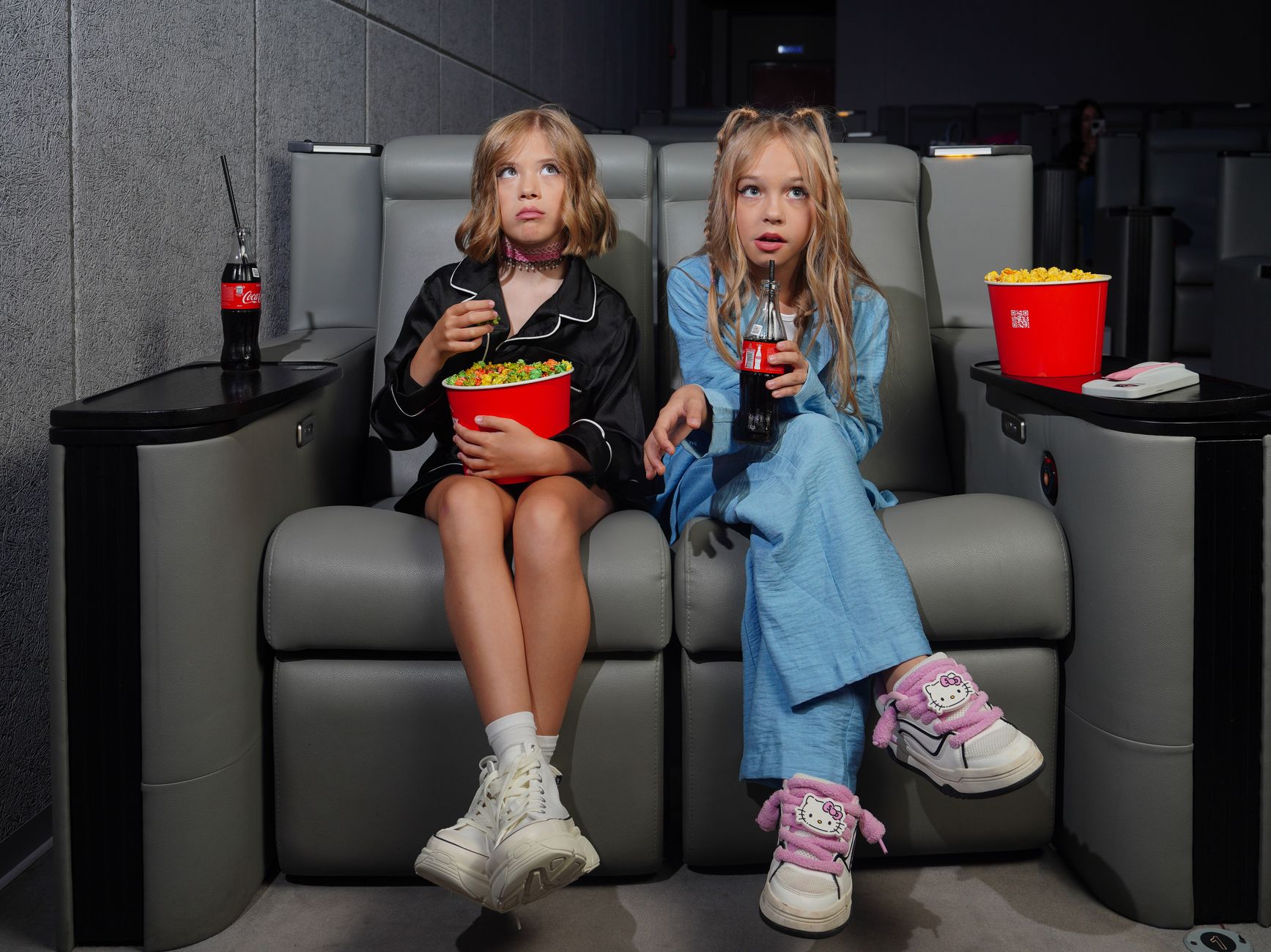 Two girls with snacks enjoying a movie in a cinema's comfy seats.