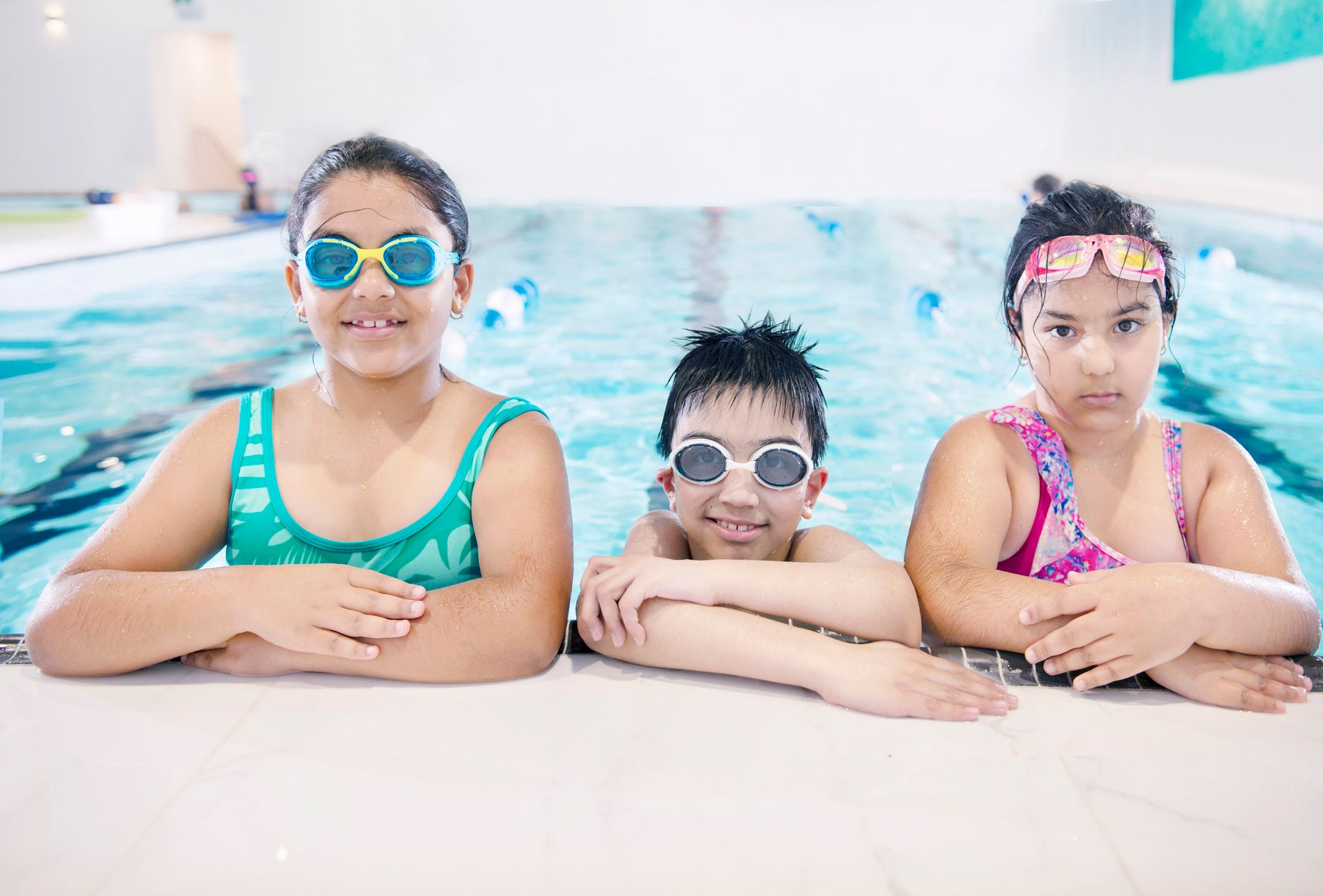 Three smiling children in swimwear enjoying a swim at an indoor pool. Perfect for lifestyle and leisure themes.