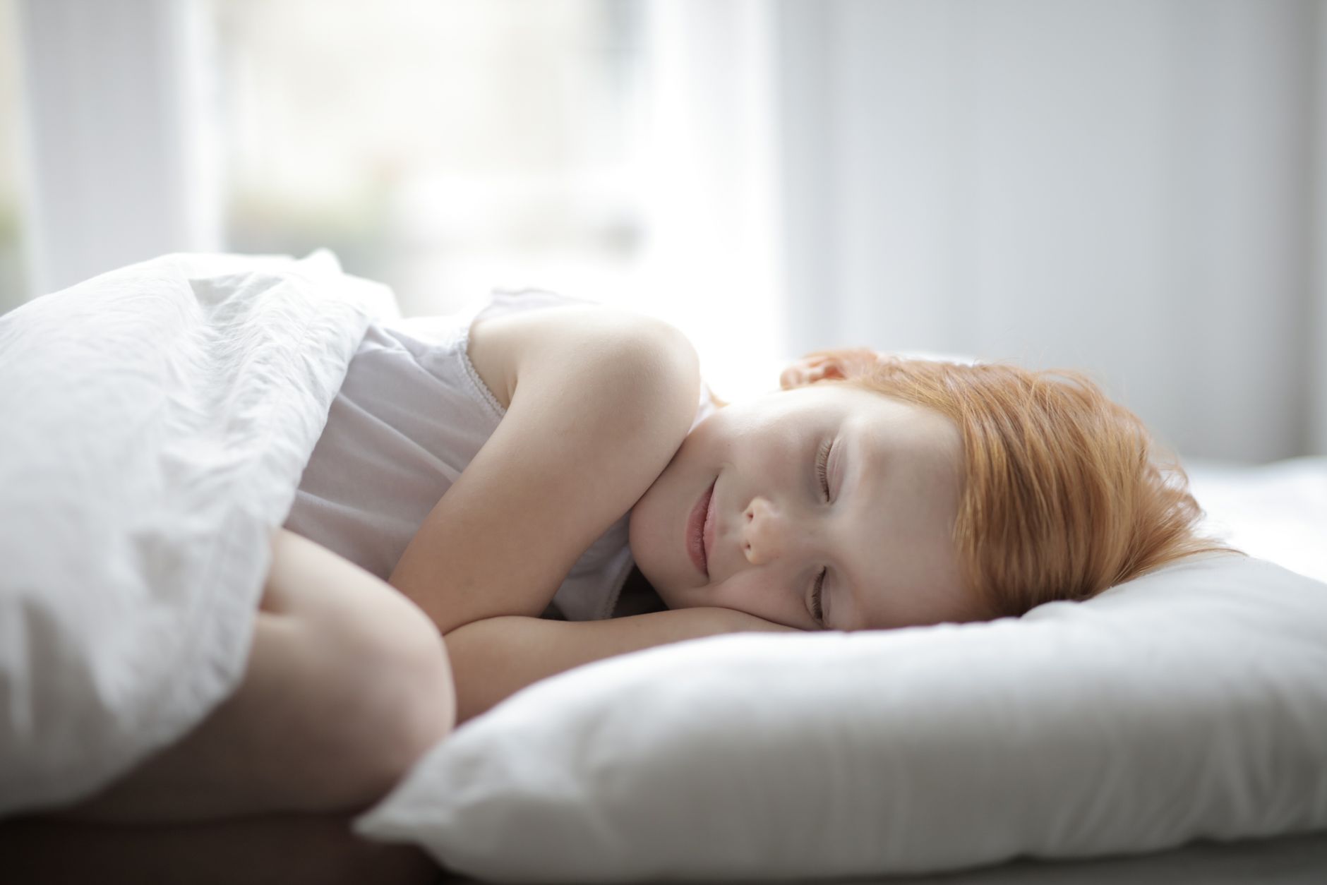 A young girl peacefully sleeping in a bright bedroom, conveying comfort and relaxation.