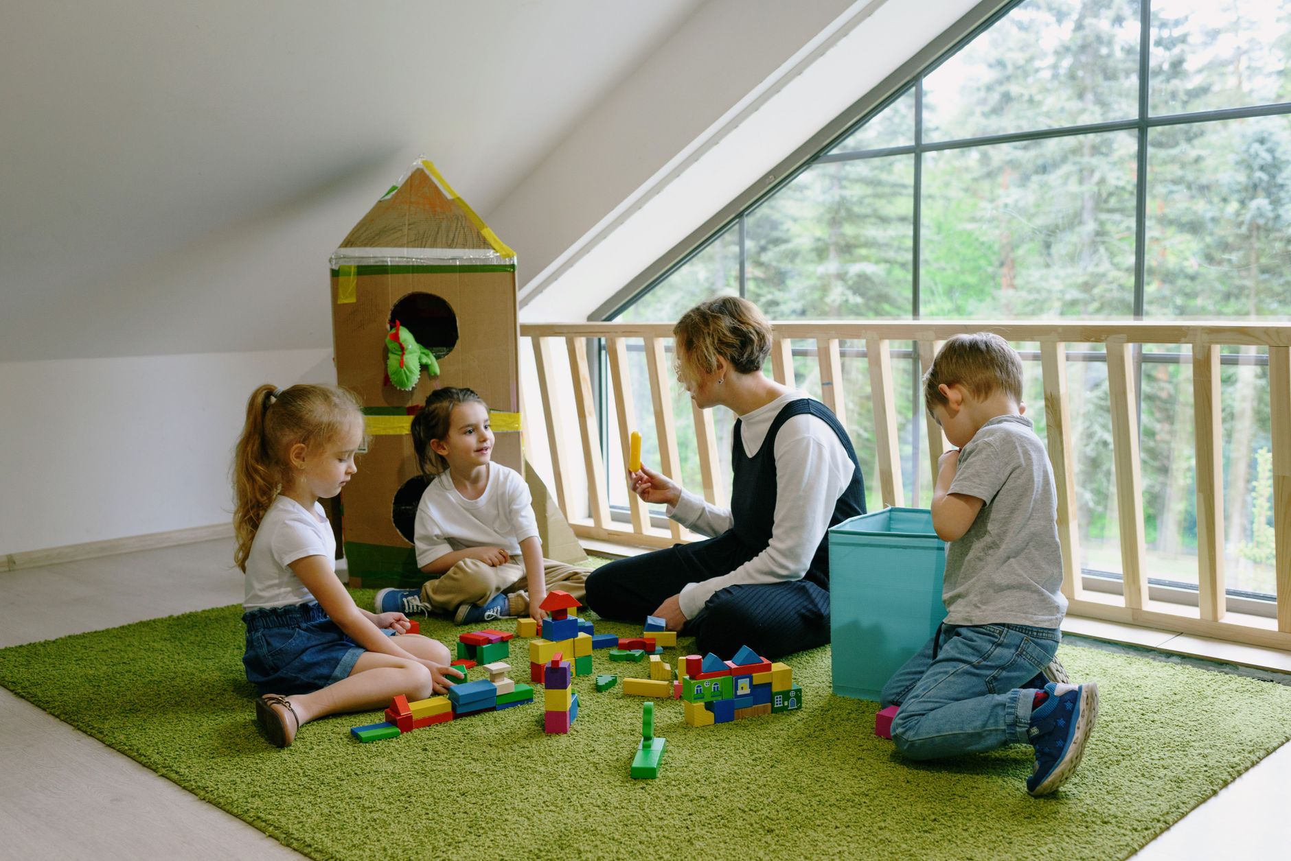 Kids in a classroom playing with colorful wooden blocks on a green carpet, guided by a teacher.