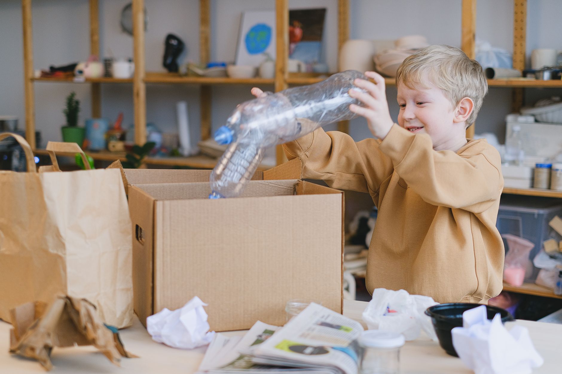 A young boy happily sorts plastic bottles into a cardboard box for recycling.