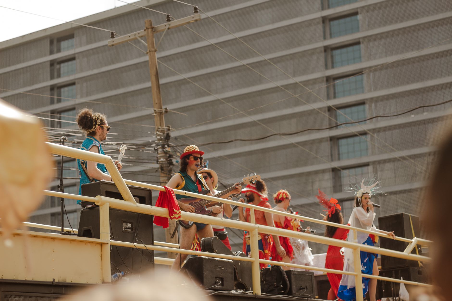 A vibrant outdoor concert with performers in colorful costumes onstage, set against a city backdrop.
