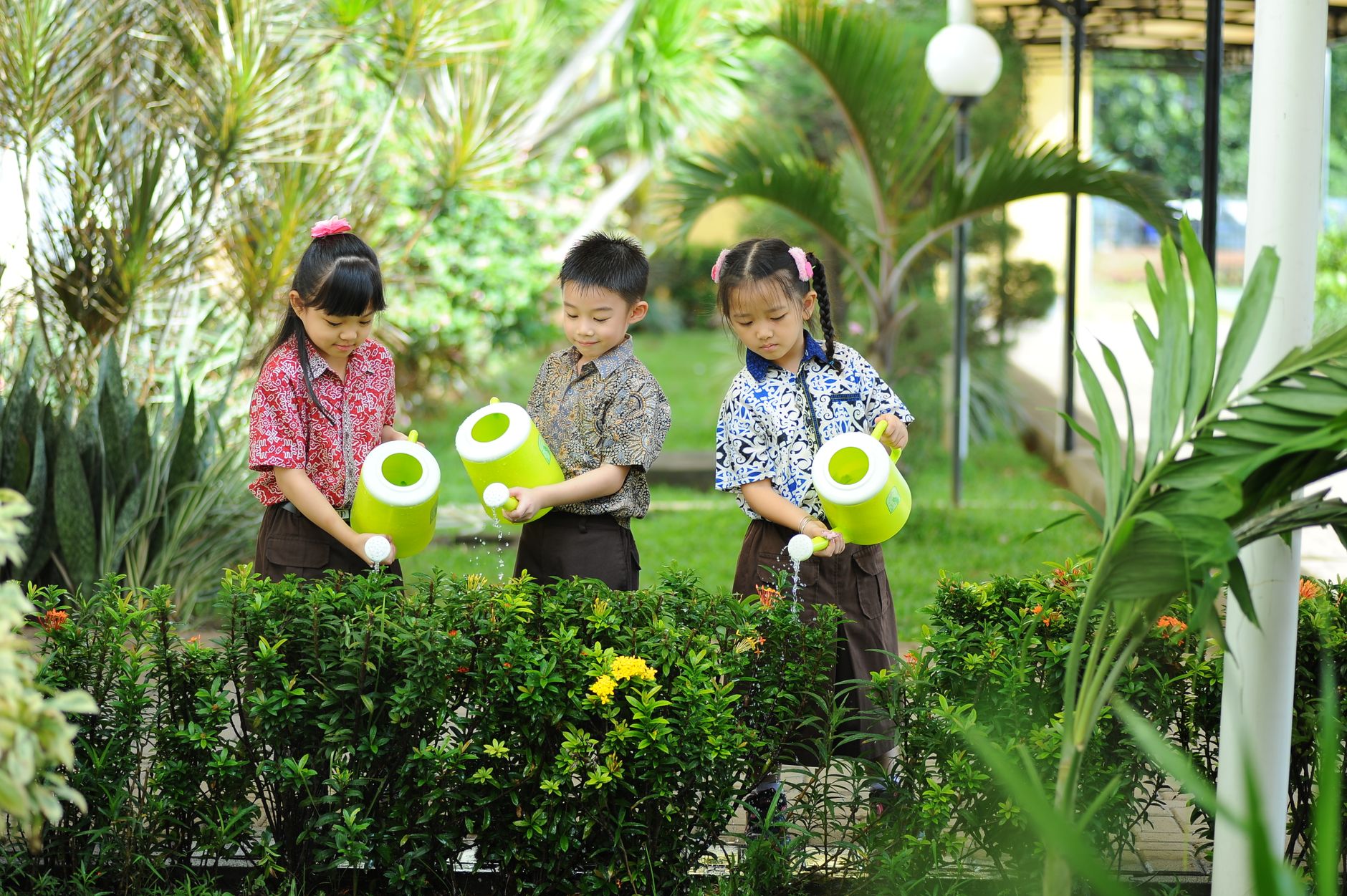 Three children in a garden watering plants with bright green watering cans, promoting teamwork and nature care.