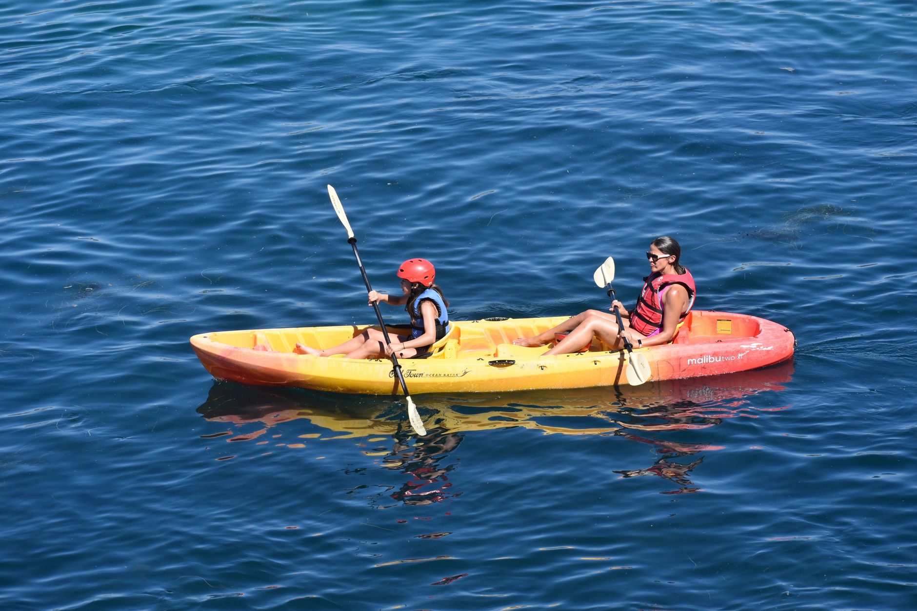 A woman and child enjoy a sunny day kayaking together on open water.