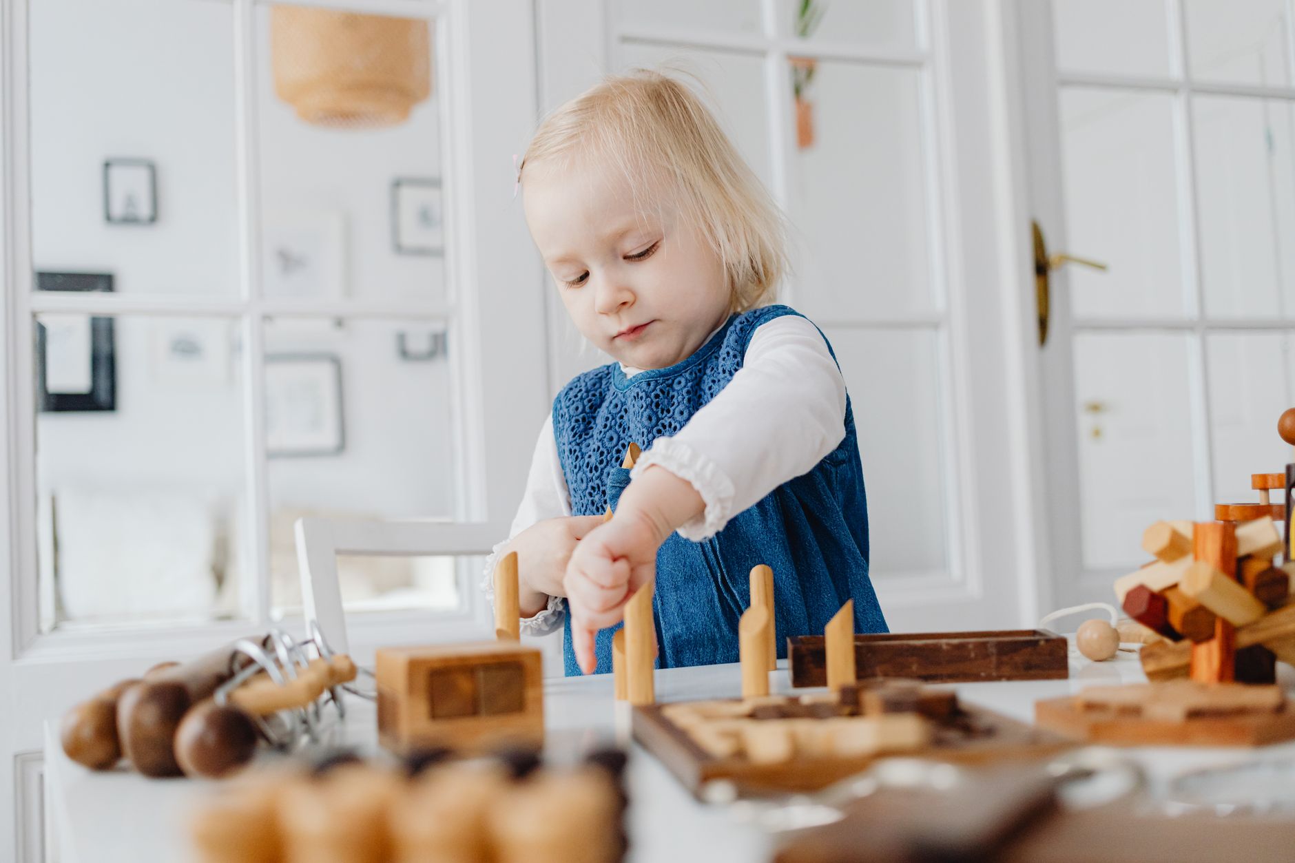 Blonde toddler focused on assembling wooden toys indoors, enhancing creativity.