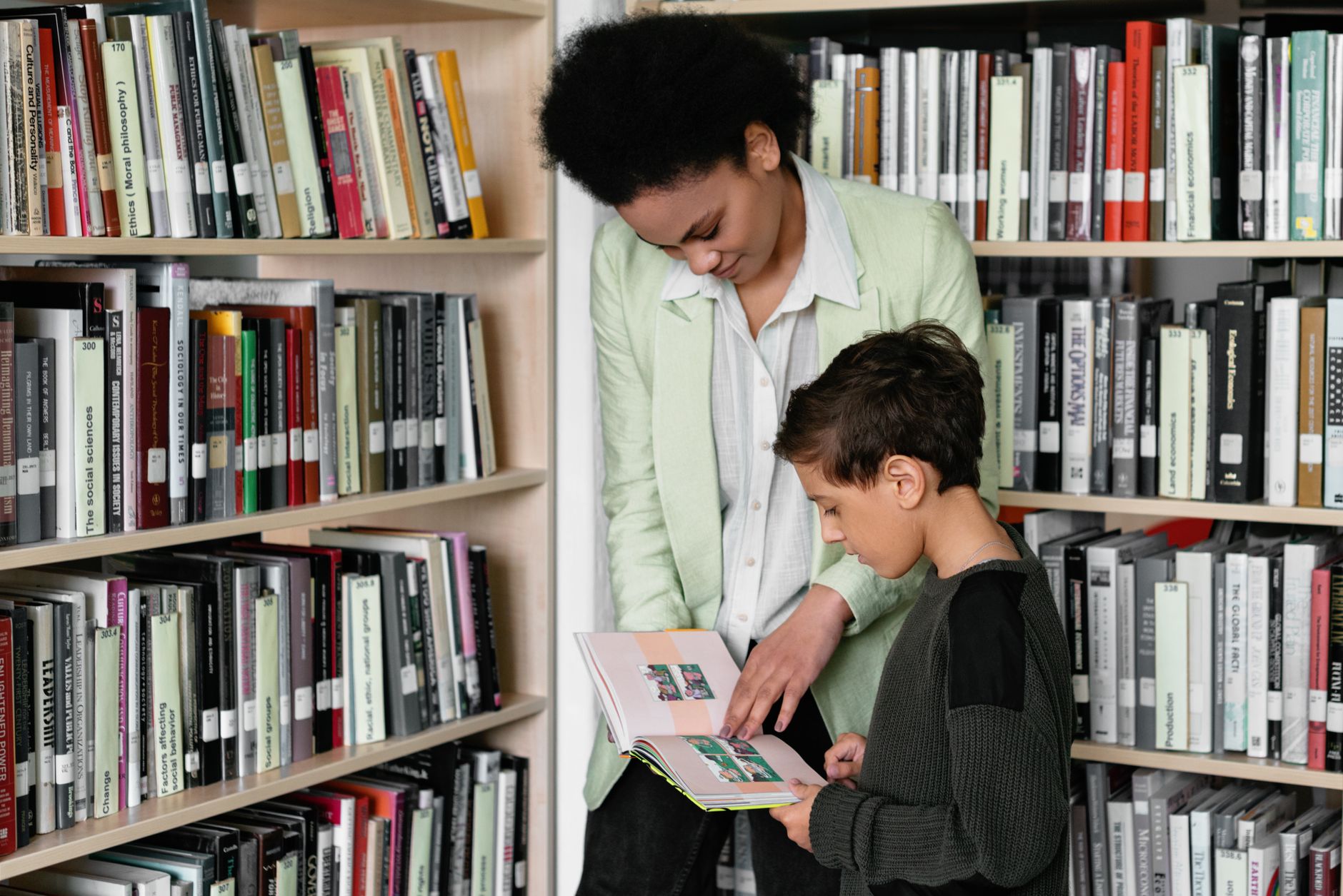 An adult helping a child read a book in a library setting, fostering learning.