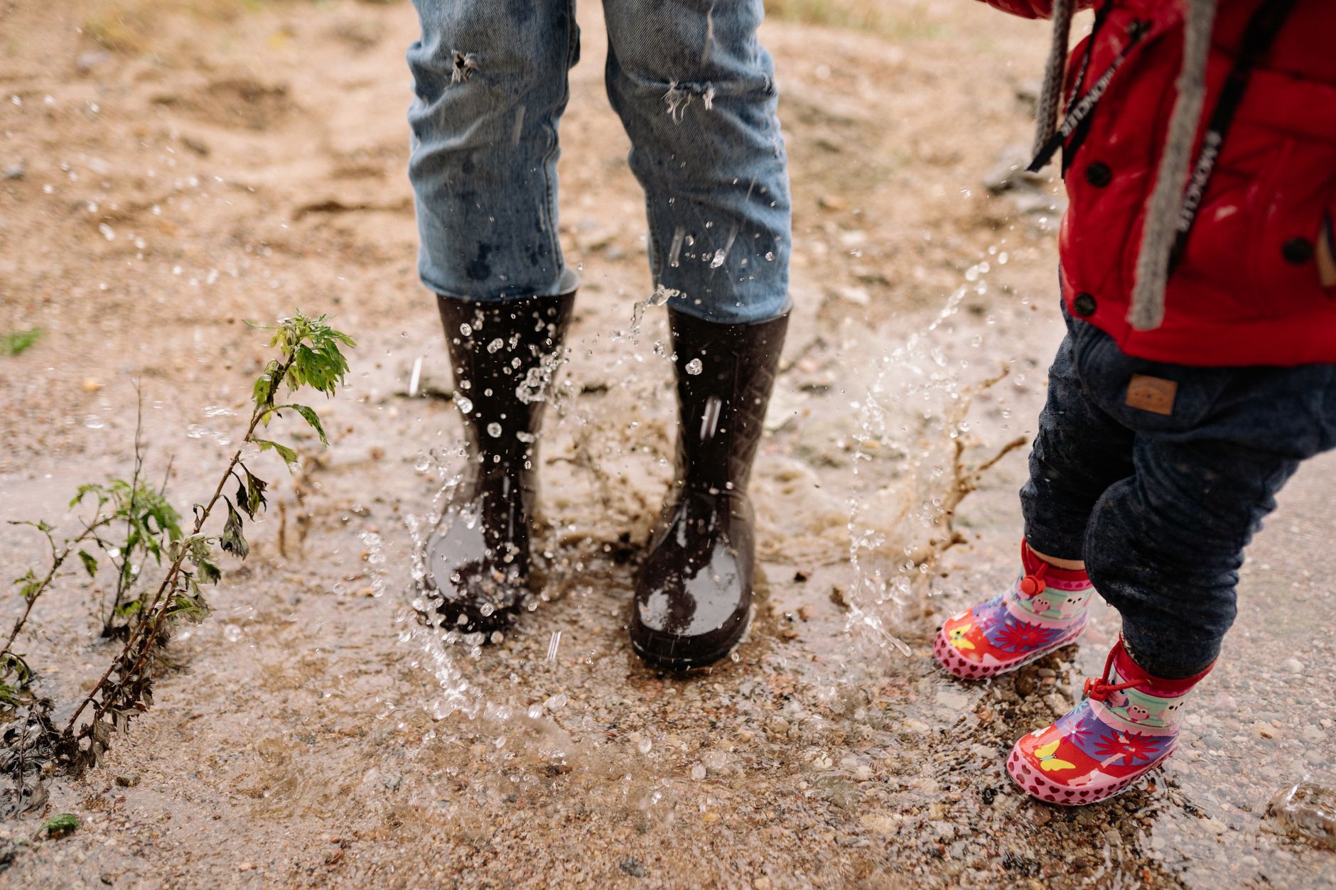 Two children enjoy splashing in water wearing rain boots outdoors.