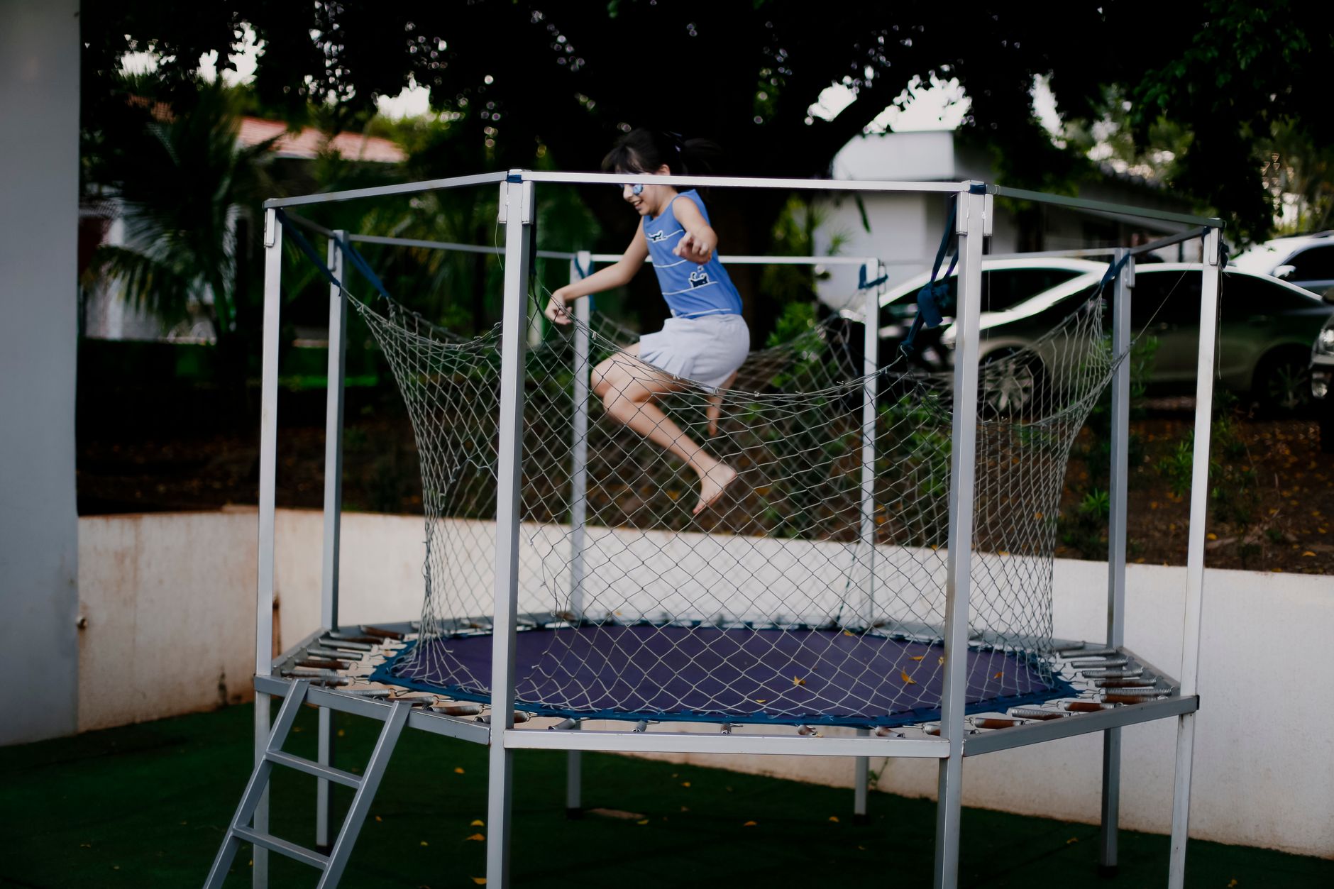 A young girl energetically jumps on a trampoline outdoors, enjoying a fun and playful moment.