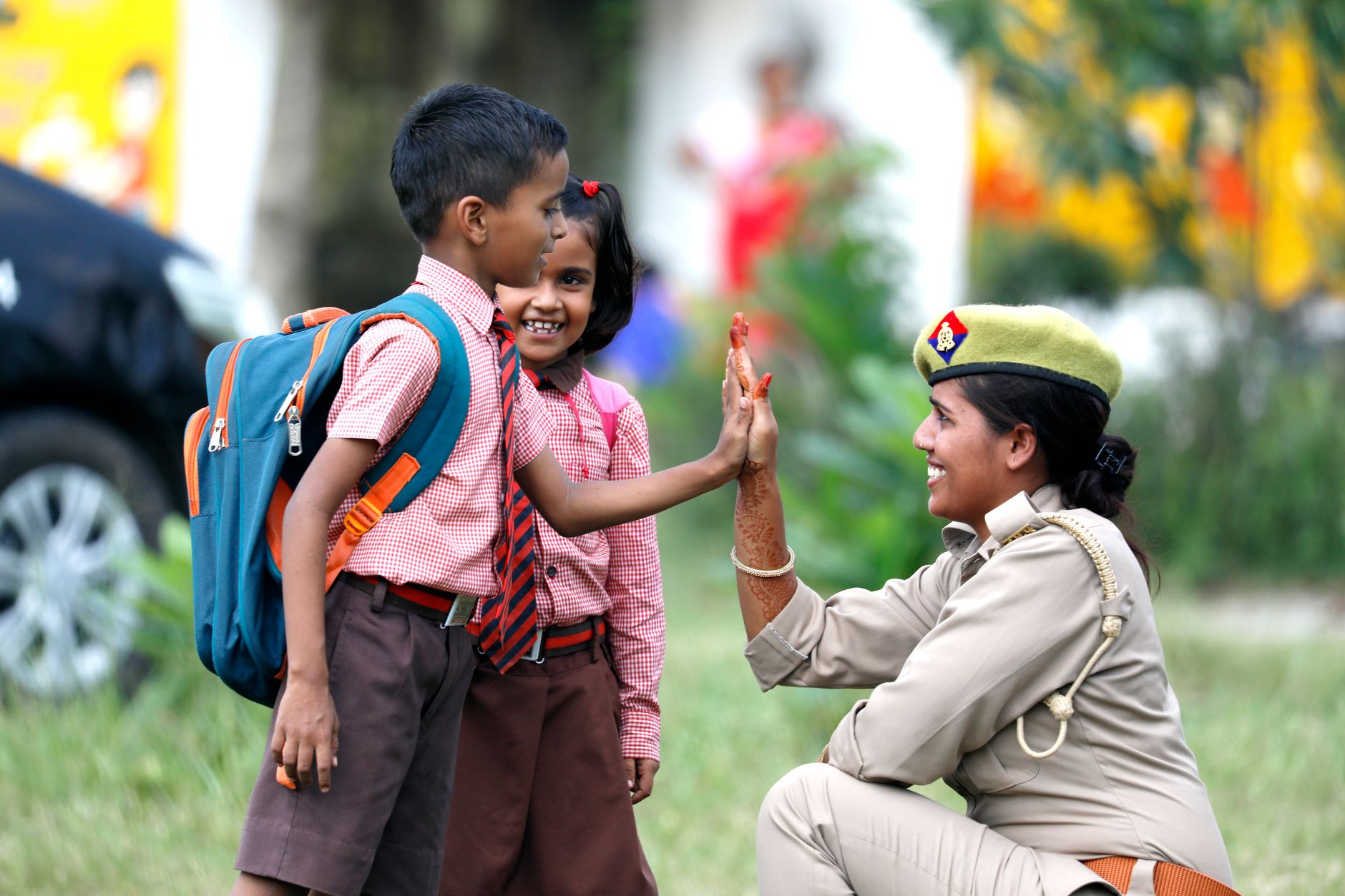A policewoman high-fives schoolchildren in uniform on a sunny day, fostering community spirit.