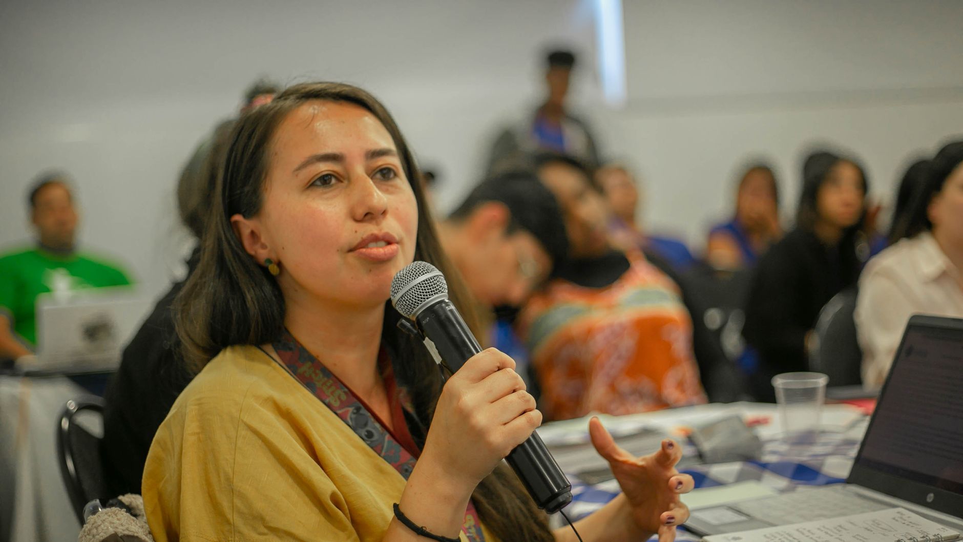 Young woman with microphone speaking during a classroom presentation with students.
