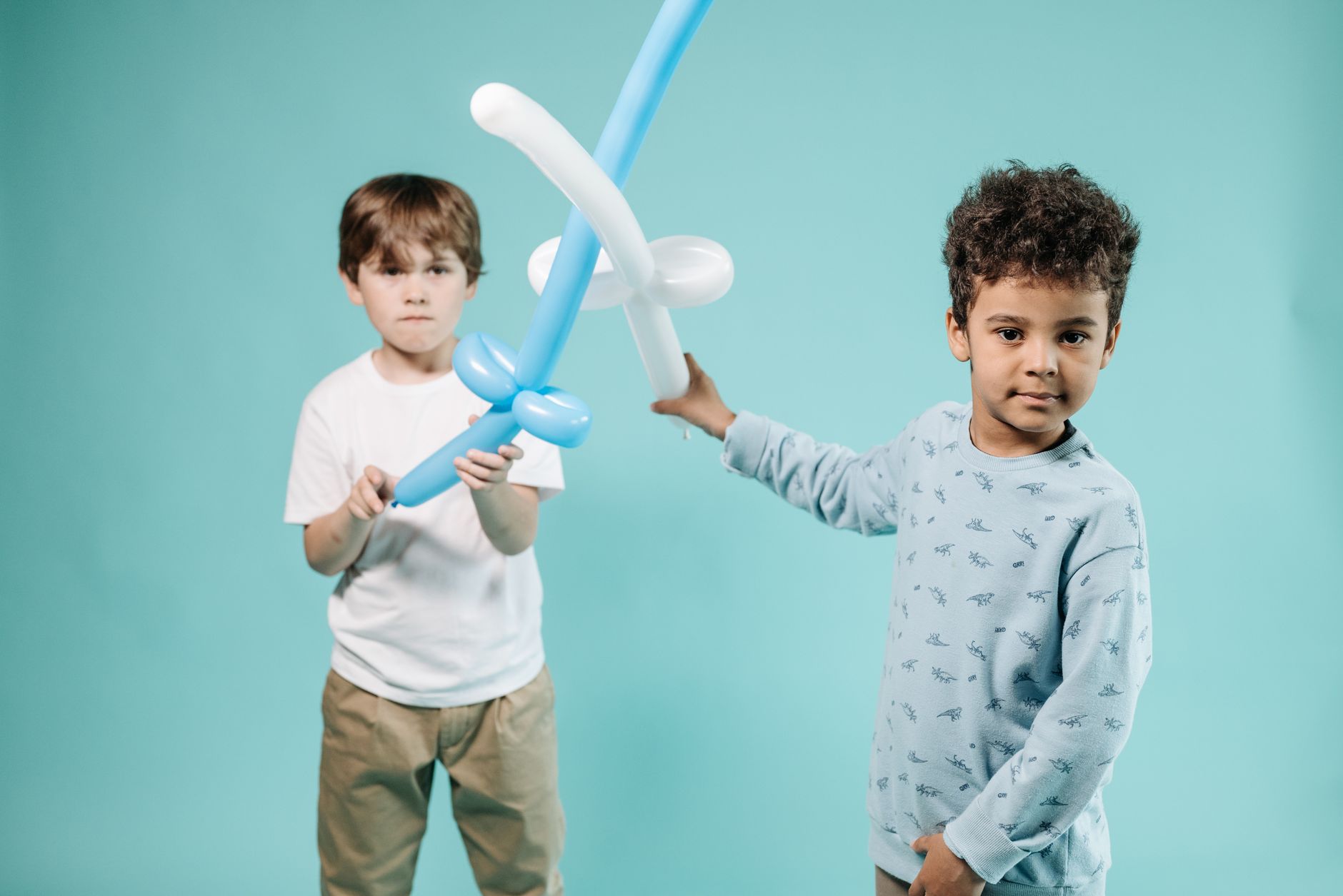 Two boys having fun with balloon swords in a playful indoor setting.