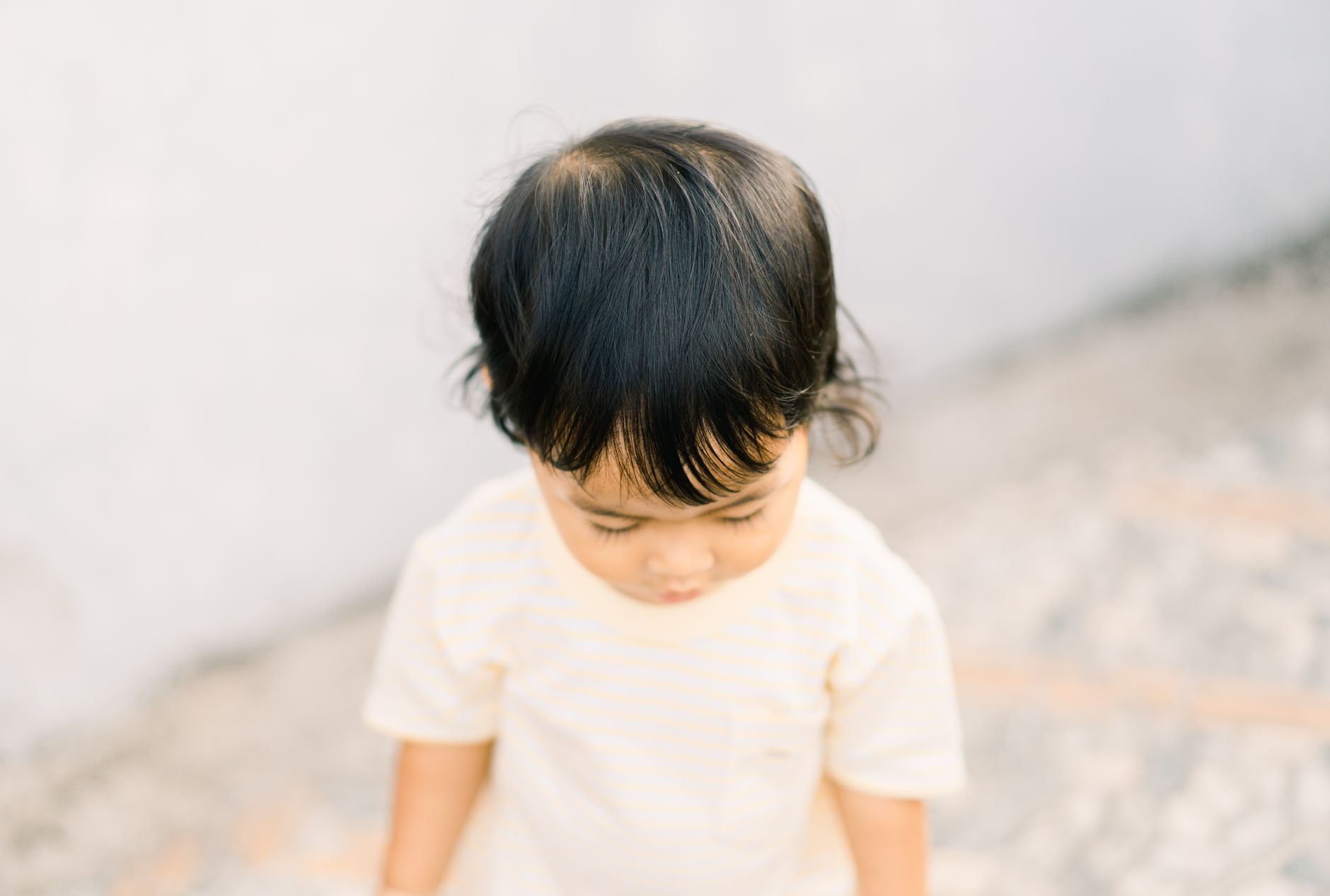 A cute child with black hair looking down, captured in soft, warm lighting.