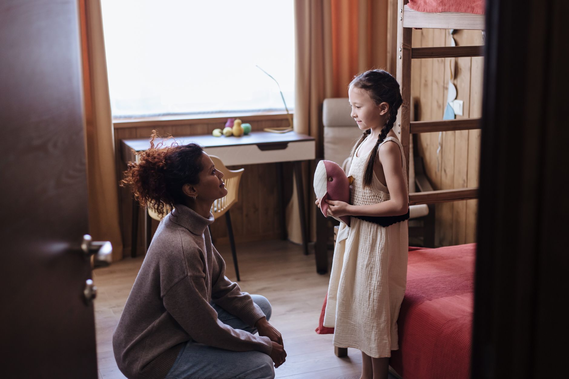 Mother kneeling and talking to her daughter in a cozy home interior, fostering a loving family bond.