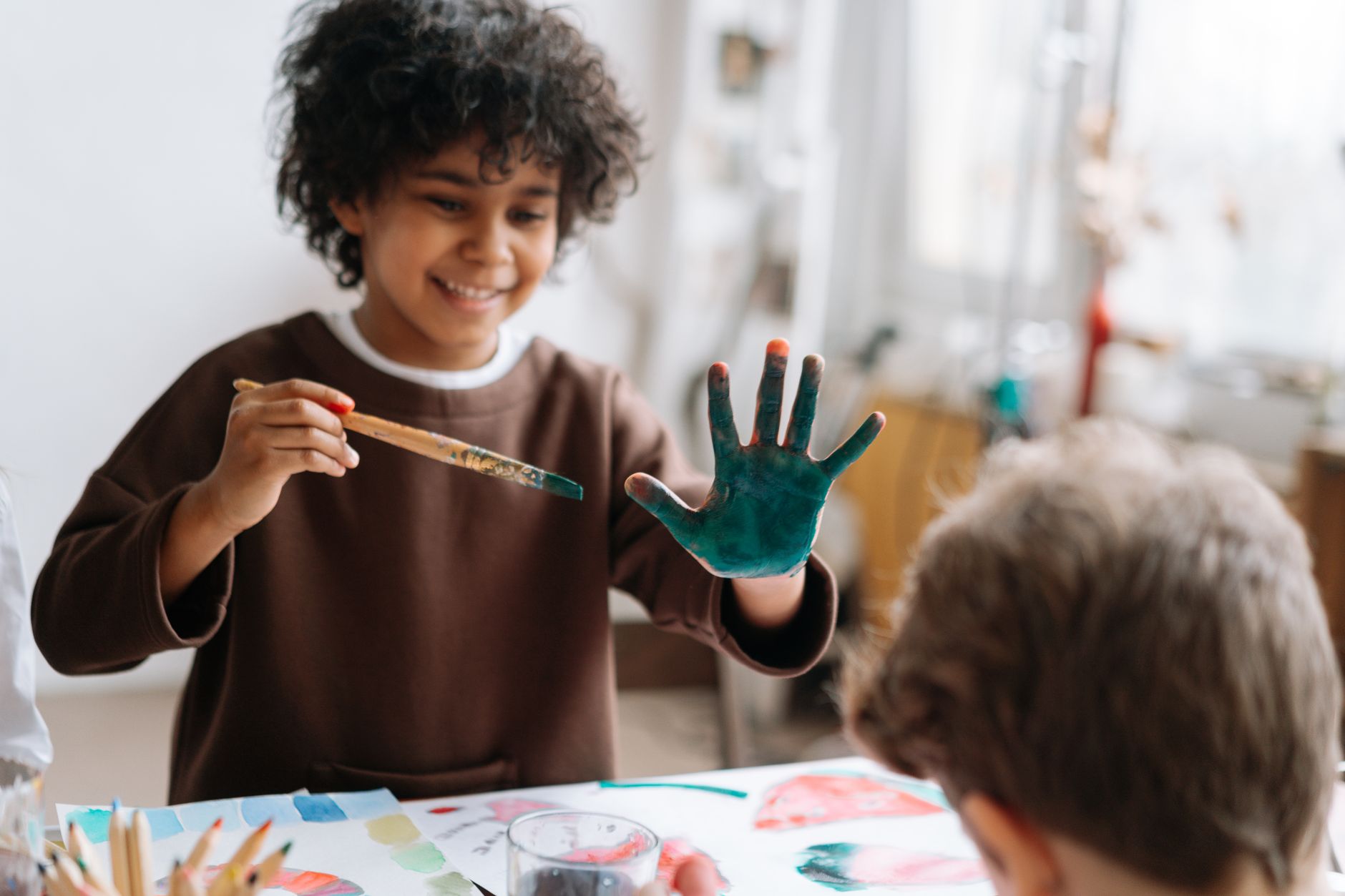 Smiling child painting with hands in an art workshop. Creative learning environment.