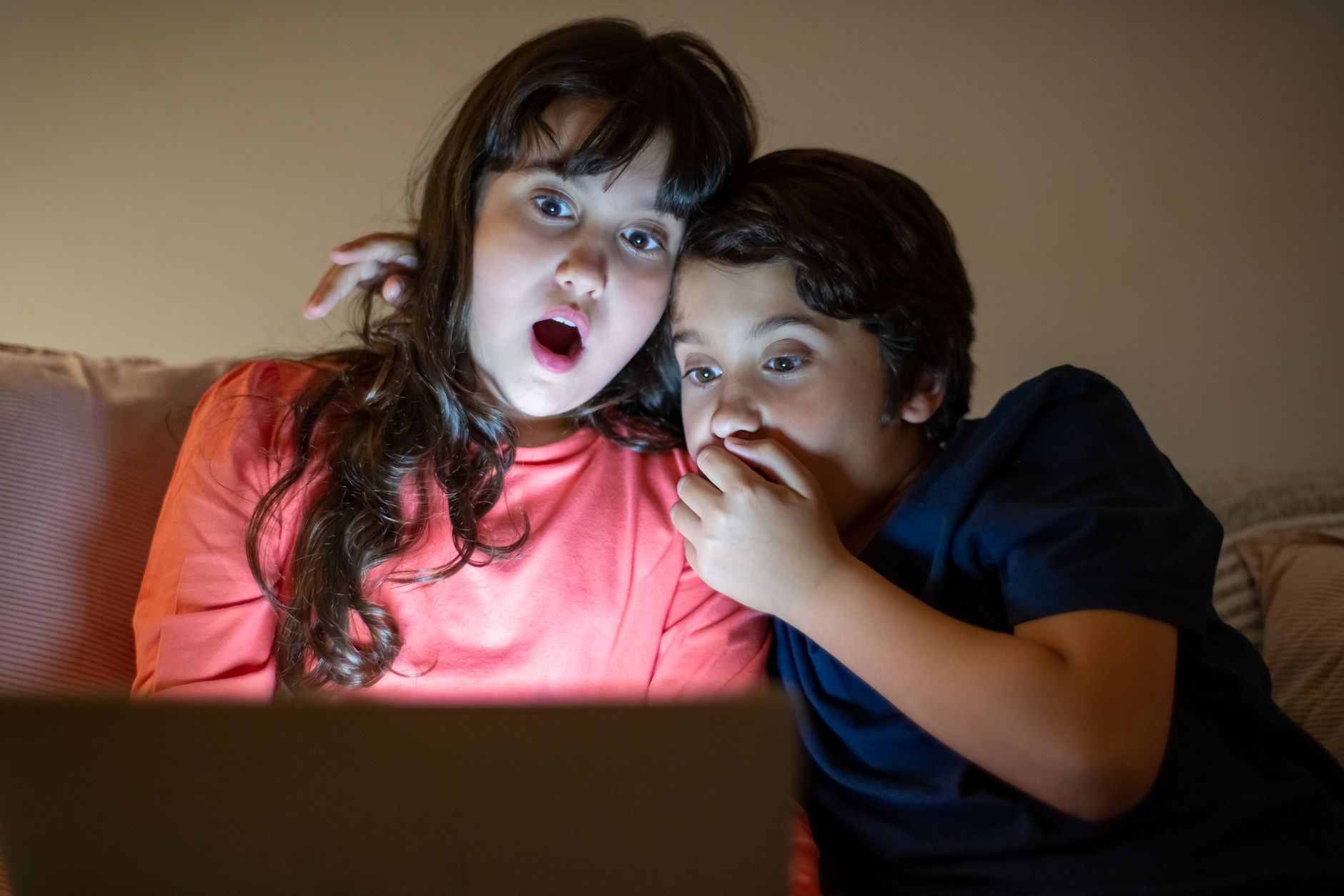 Two siblings experiencing a shocking moment while watching a tablet together at night.