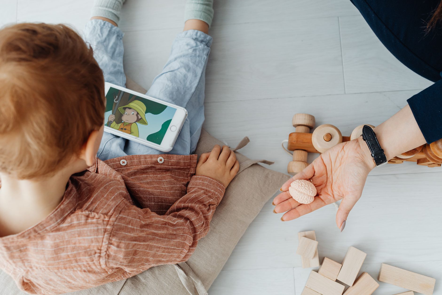 A mother and child sitting on the floor watching a cartoon on a tablet.