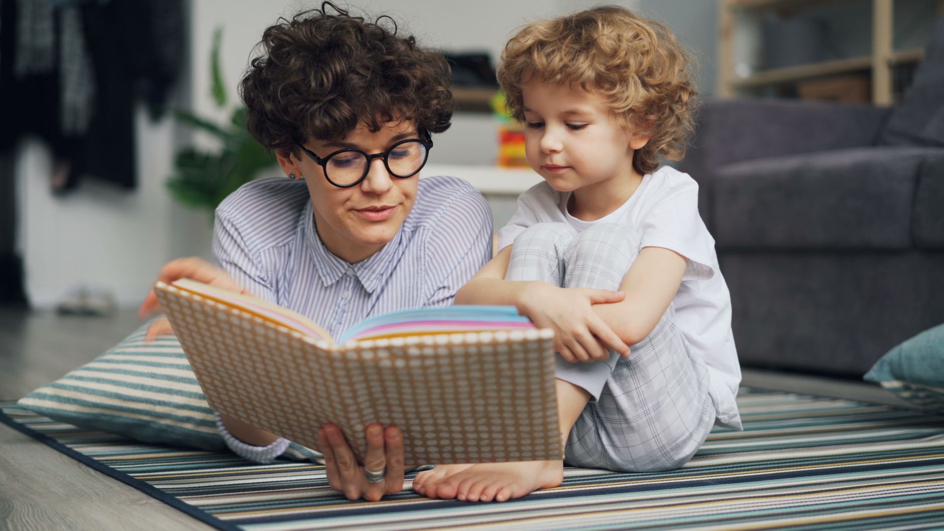 Mother and young son lying on carpet, engaged in reading a book together happily.