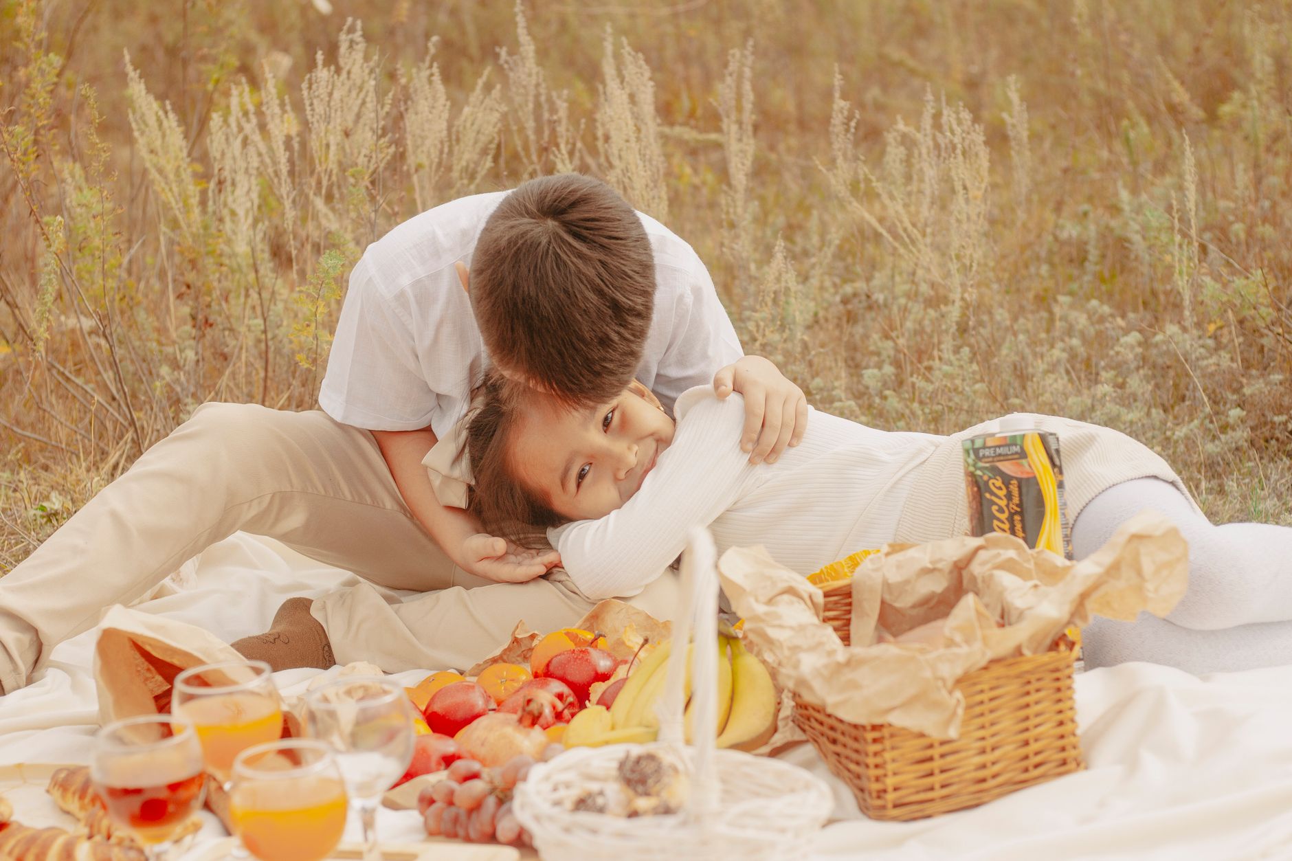 A boy and girl enjoying an outdoor picnic with fruits and drinks during autumn.