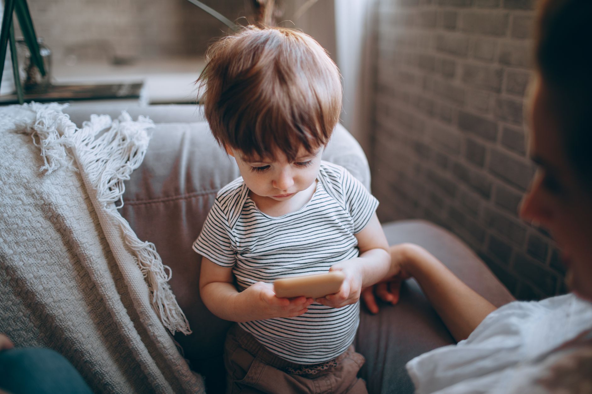 A young child engaging with a smartphone while sitting indoors with a parent nearby.