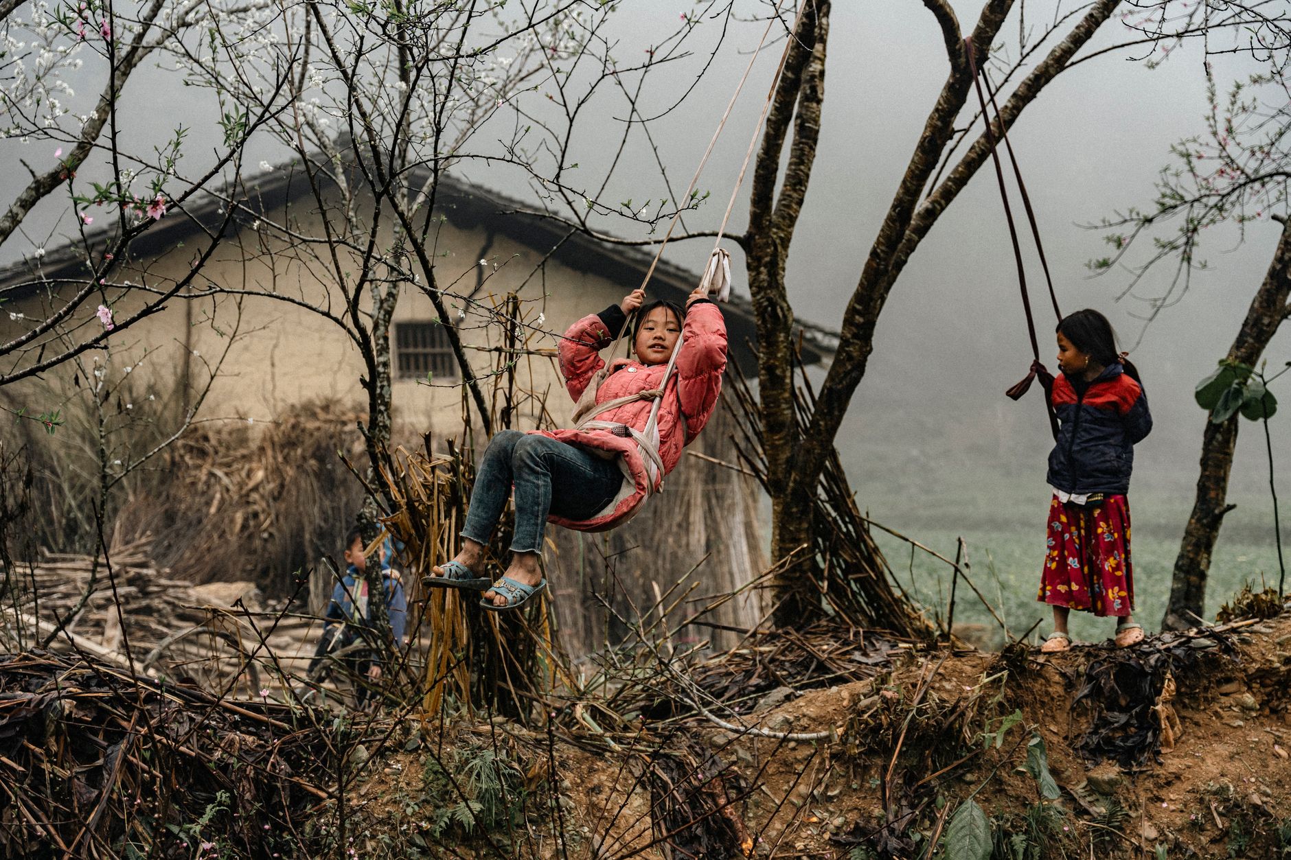 Two children enjoy playing on swings in a rural village, showcasing joy and nature.