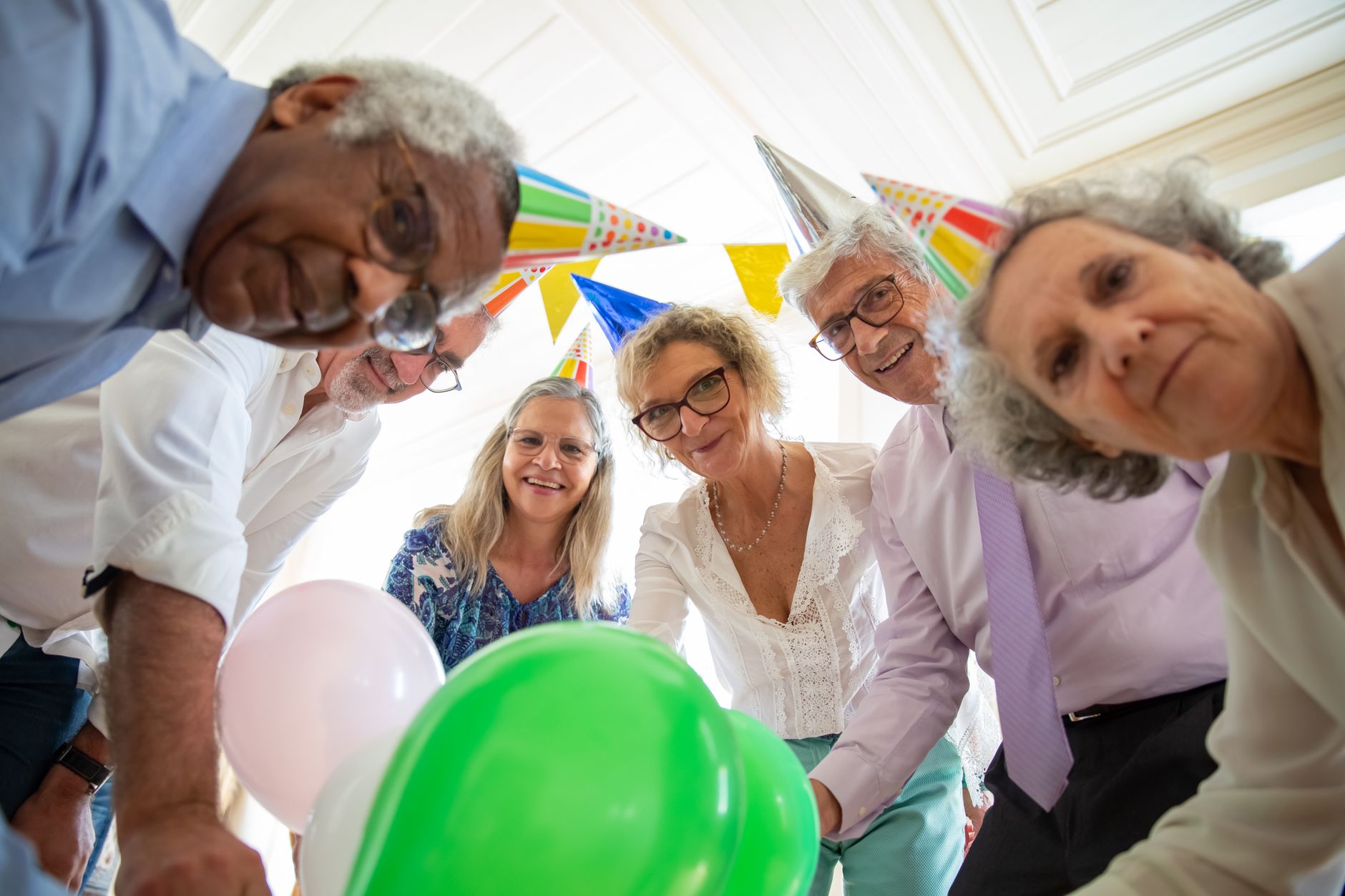 Group of seniors celebrating indoors with balloons and party hats, sharing a joyful moment together.