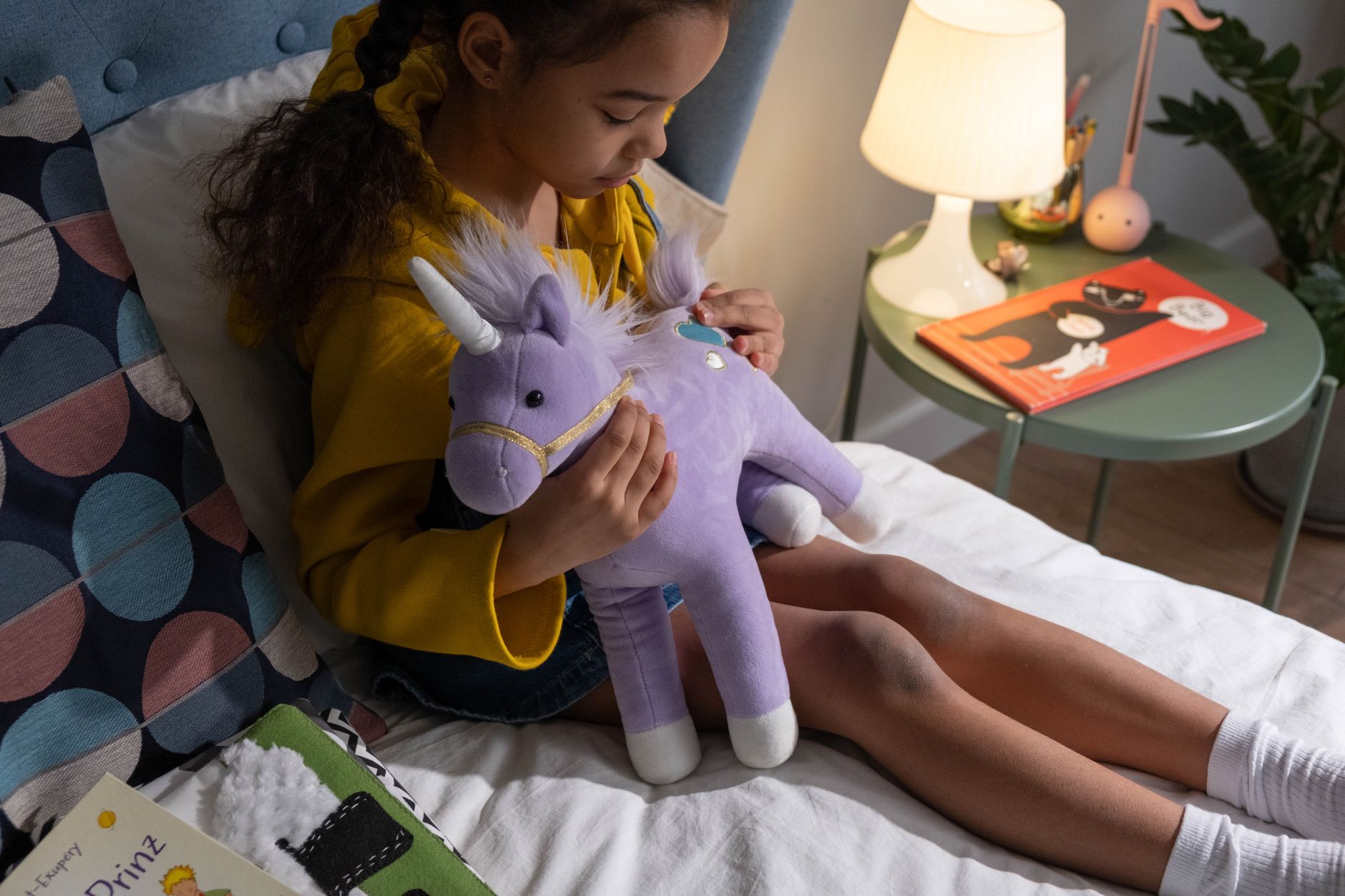 A child plays with a unicorn stuffed animal on a bed in a cozy bedroom setting.