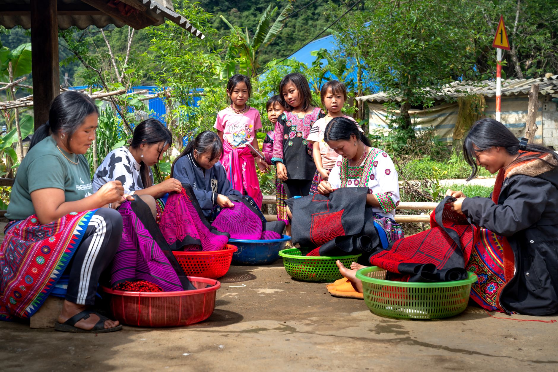 Women and children working on textile crafts outdoors, showcasing traditional handmade fabrics.